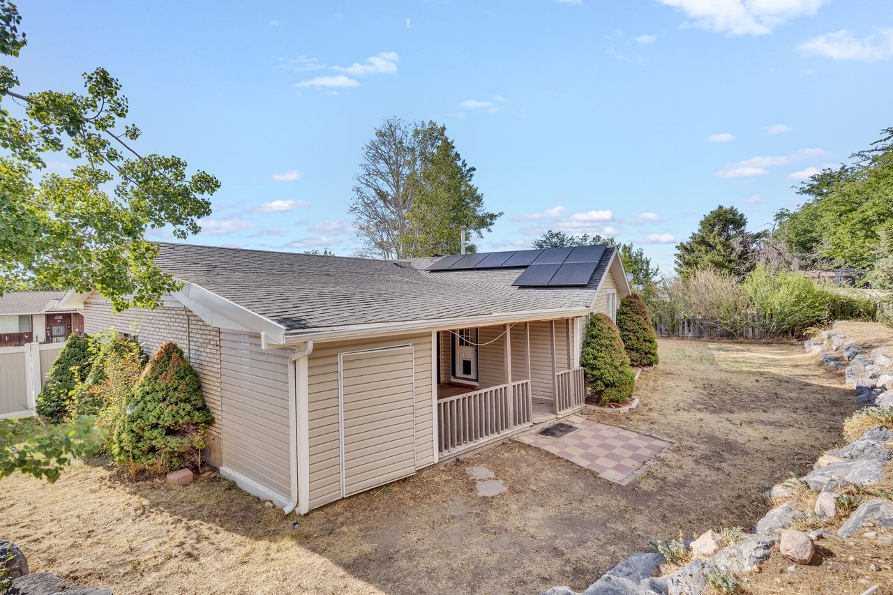 Exterior with tan siding and brick accents, featuring a covered porch with railing, a shingle roof, and visible solar panels