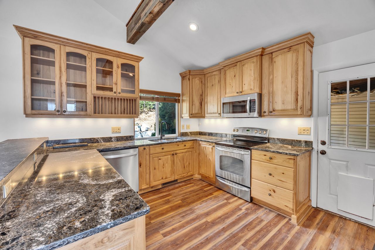 Kitchen featuring wood-finish flooring, natural wood cabinetry, dark patterned countertops, and stainless steel appliances