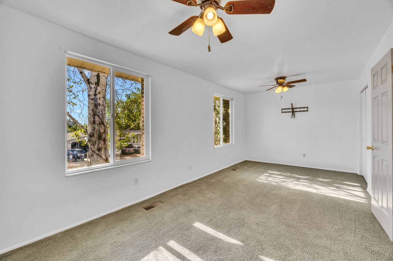 Spacious room featuring light-colored carpet, two windows with white trim, and two ceiling fans with integrated lighting