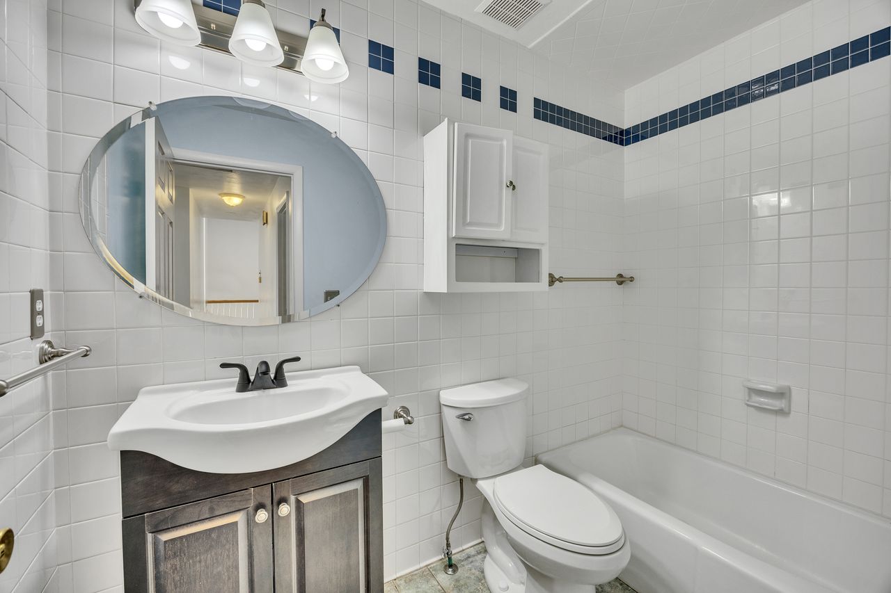 Bathroom featuring white tiled walls with blue accent trim, a white ceramic bathtub, and a built-in toilet