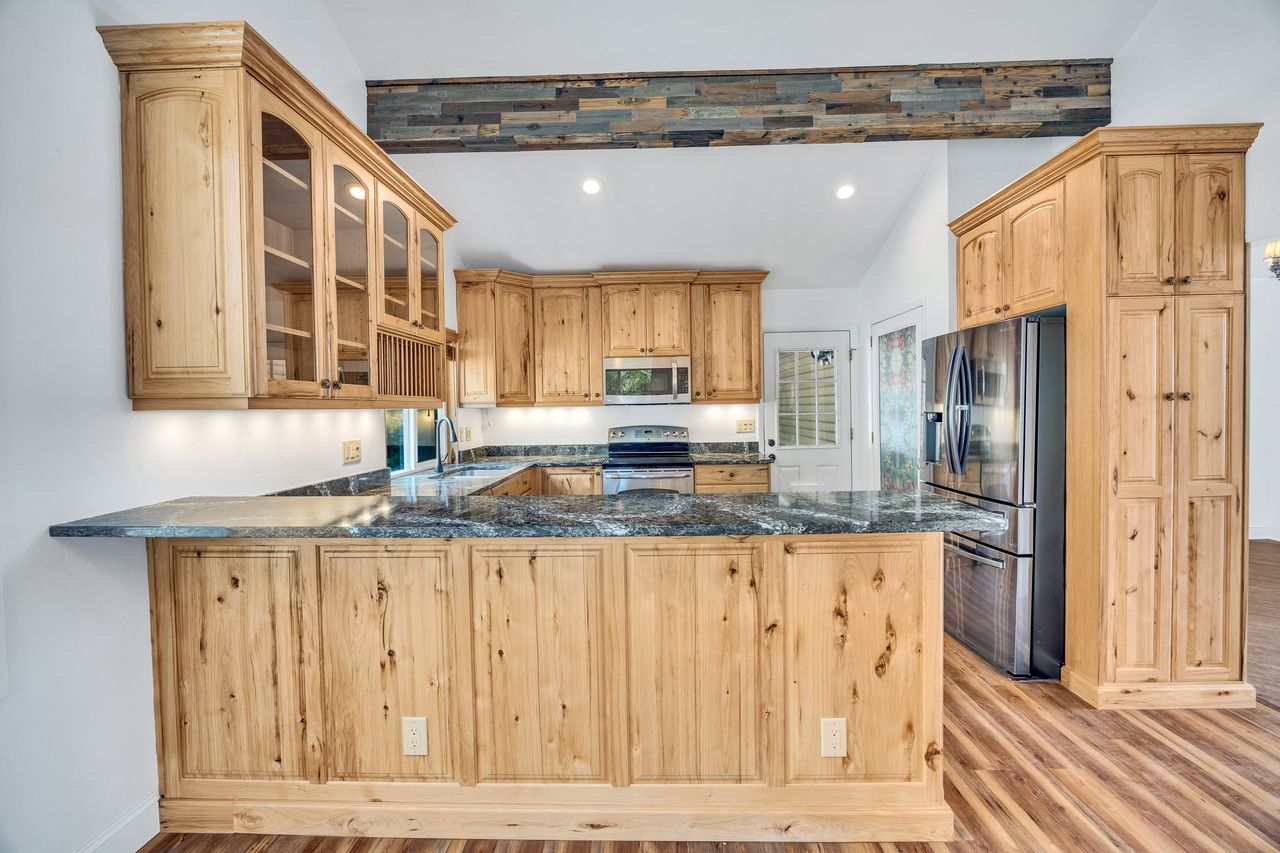 Kitchen featuring light wood cabinetry with glass-front uppers, dark stone countertops, stainless steel appliances, and wood-finish flooring