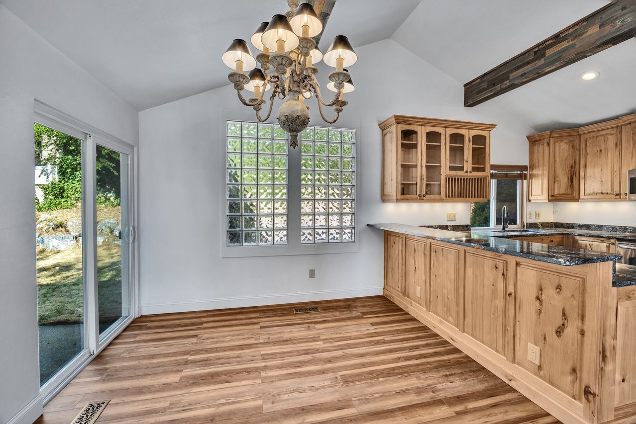 Open-concept kitchen and dining area featuring wood-finish flooring, a vaulted ceiling, and a prominent decorative chandelier
