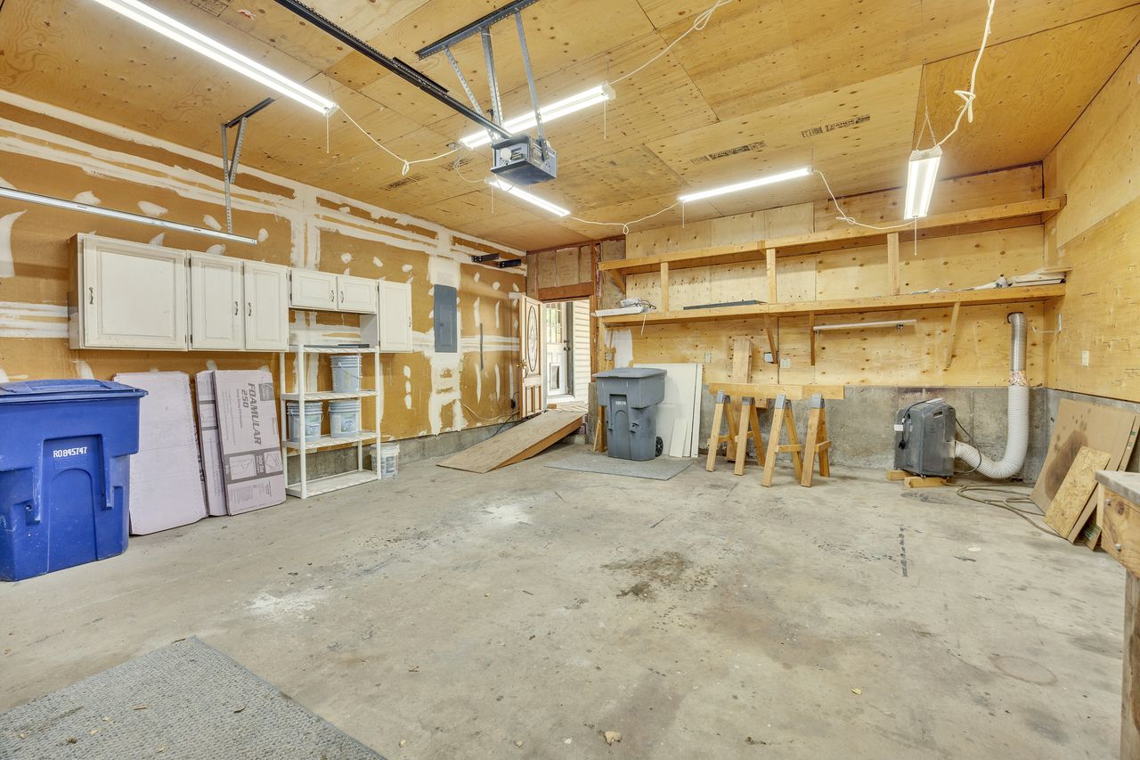 Garage interior featuring a concrete floor, plywood walls, exposed ceiling joists, and fluorescent lighting