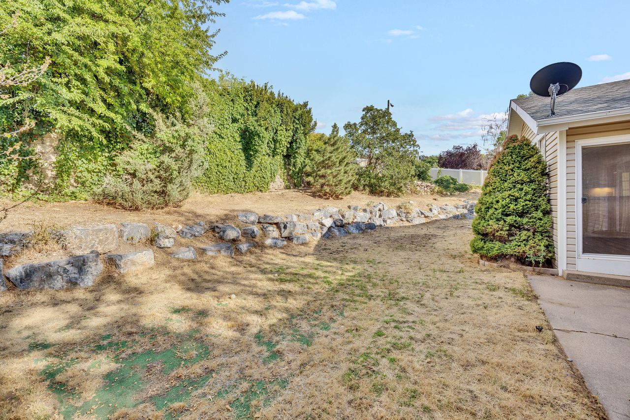 Expansive backyard with a rock retaining wall and mature perimeter plantings