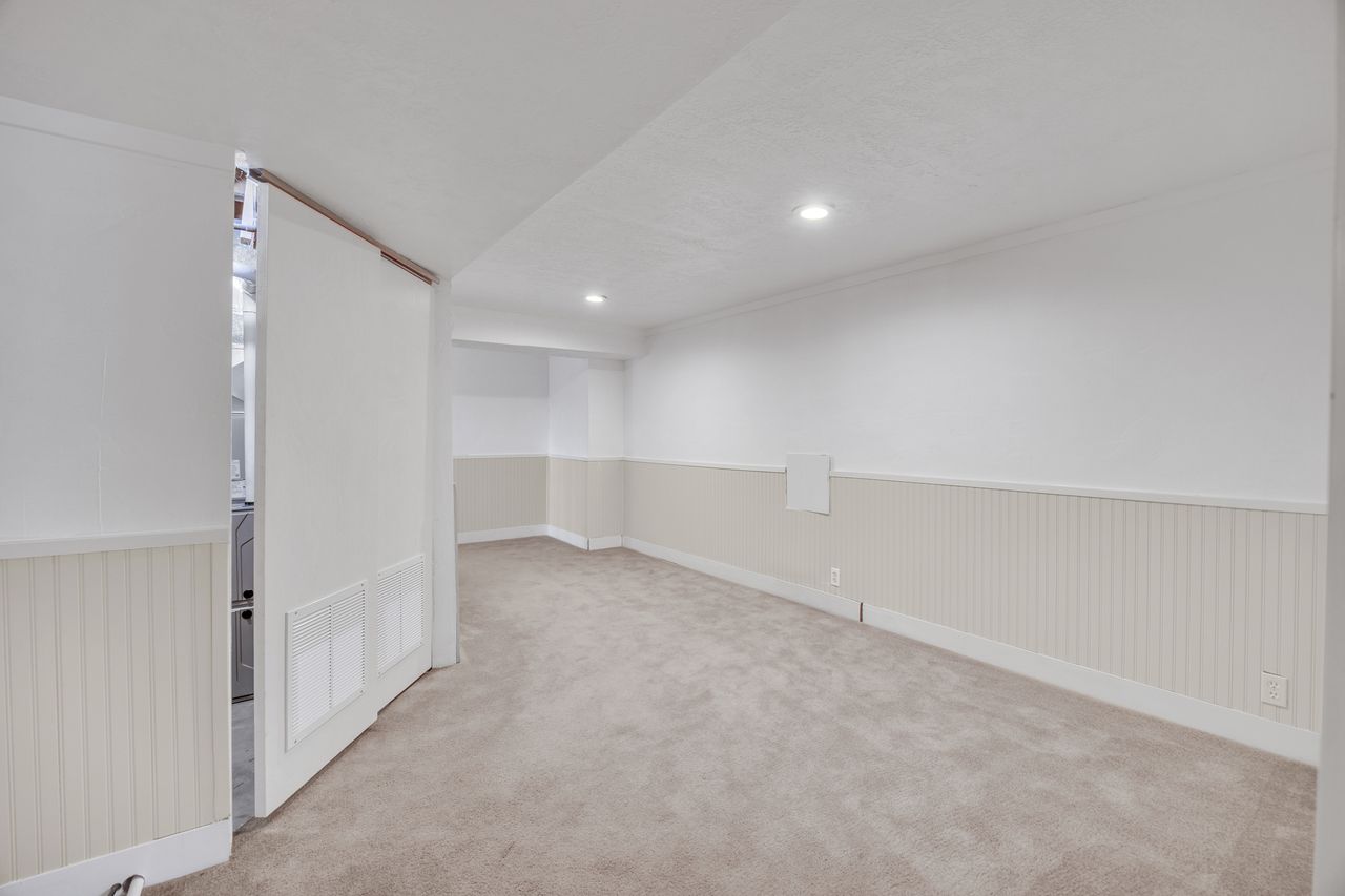 Spacious room featuring neutral carpeting, white walls with beadboard wainscoting, and recessed lighting