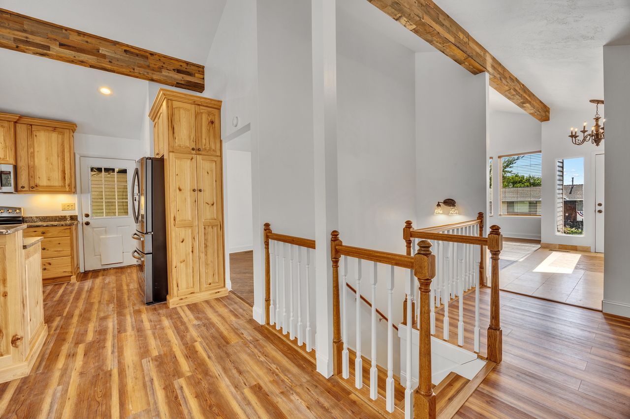 Vaulted ceilings with exposed wood beams, wood-finish flooring, and a kitchen featuring natural wood cabinetry and a side-by-side refrigerator
