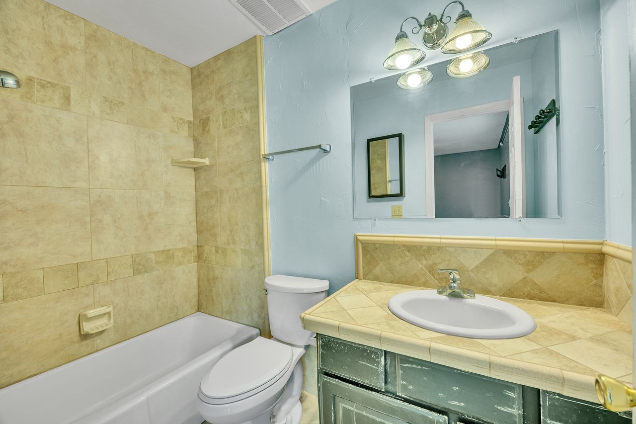 Bathroom featuring a bathtub with tile surround, a single vanity with a tiled countertop, and a wall-mounted mirror