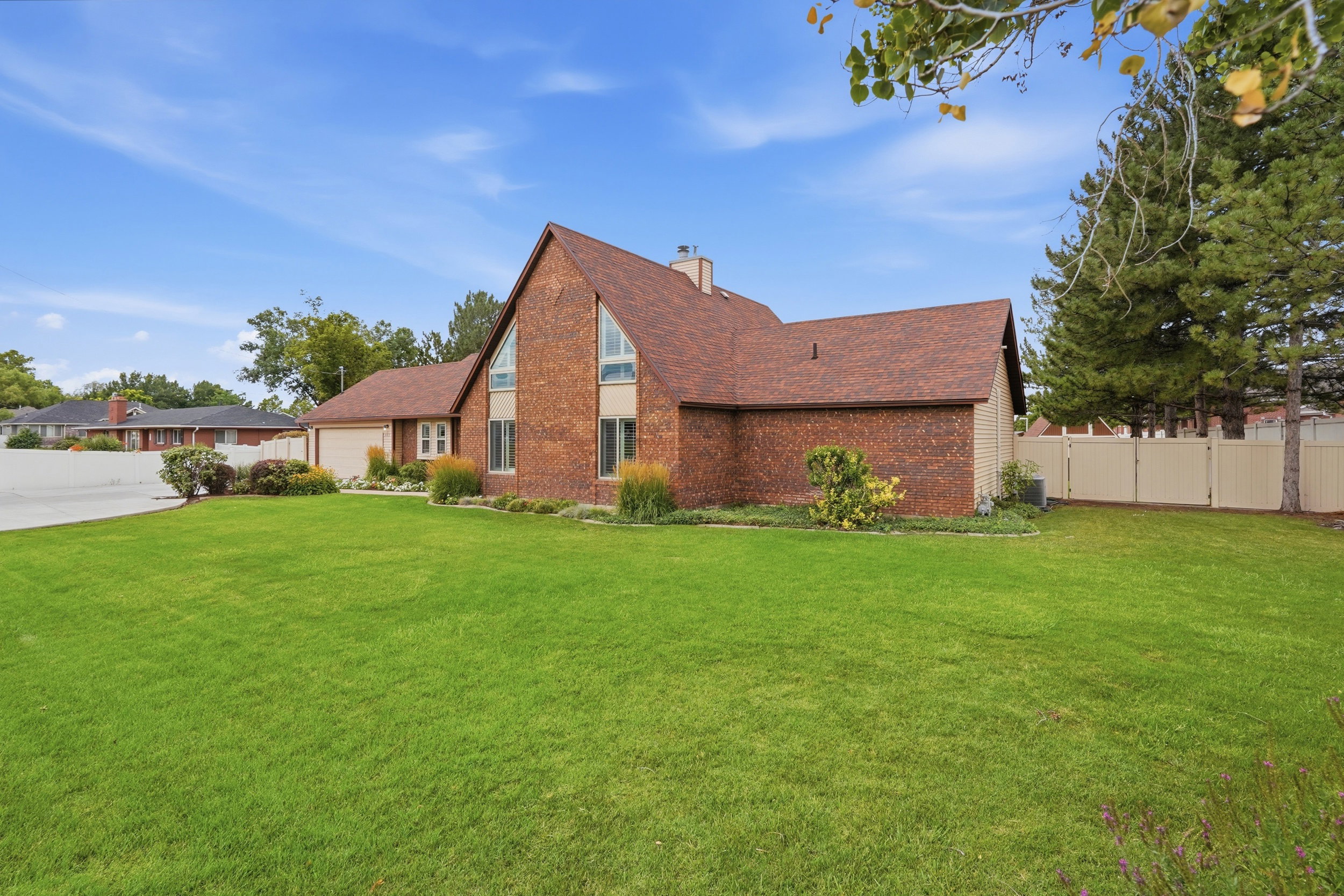 Brick exterior featuring an expansive front lawn, mature landscaping, an attached garage, and a peaked roofline