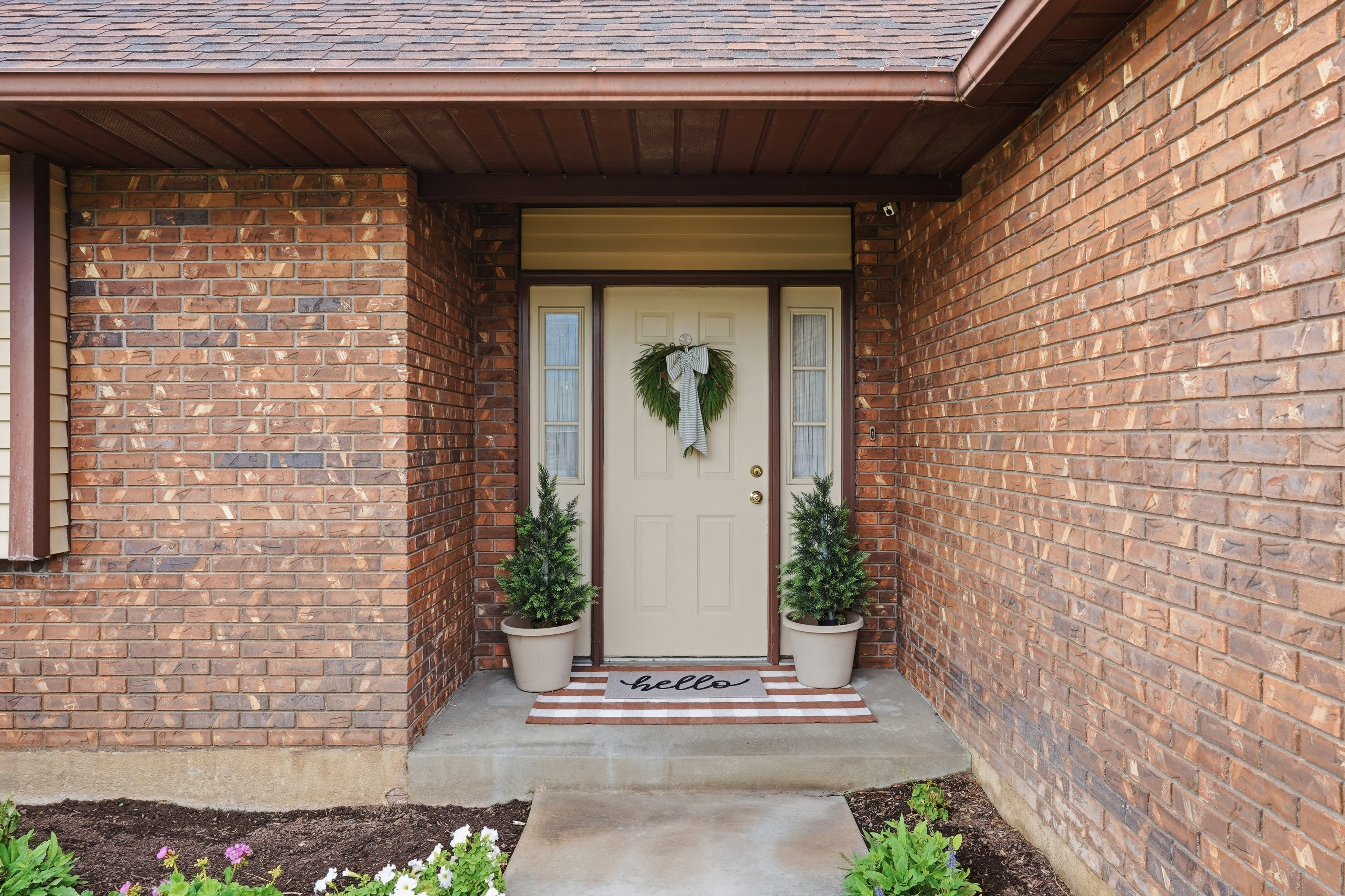 Brick exterior featuring a covered entry, neutral-toned front door, and flanking sidelight windows