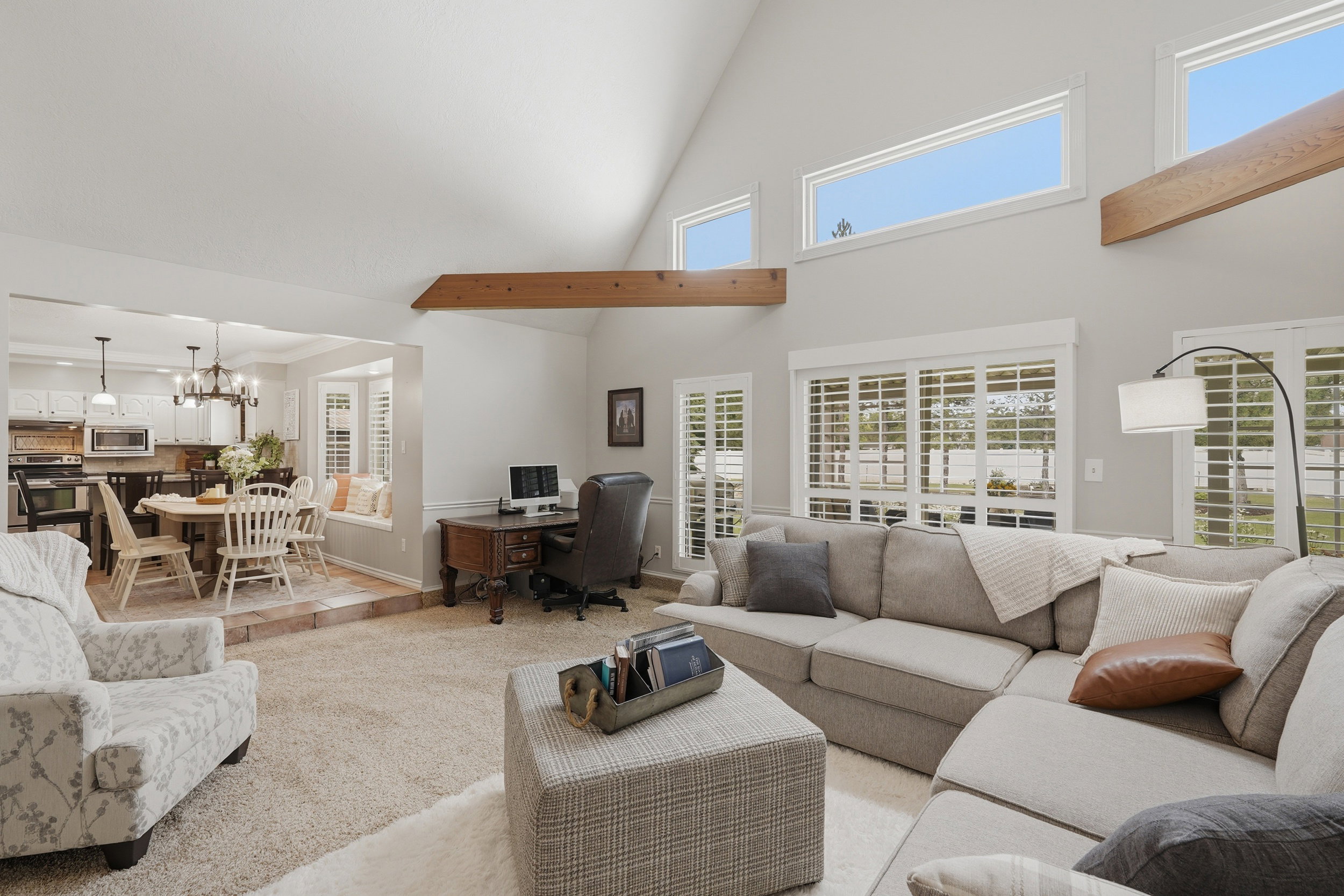 Vaulted ceilings with exposed wood beams, plantation shutters, high transom windows, and a carpeted living area
