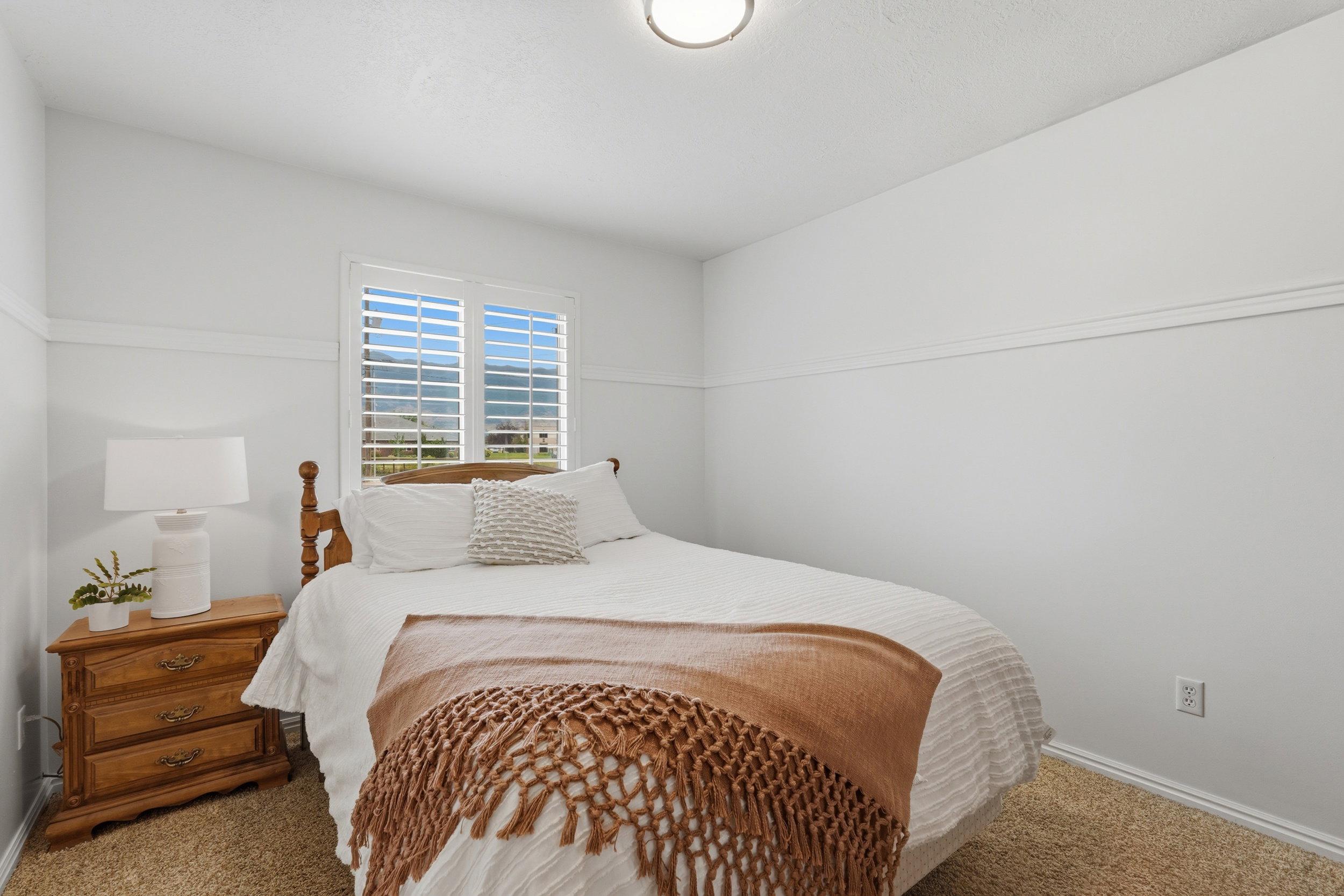 Bedroom featuring a window with white louvered shutters, light-colored wall paint, white trim, and textured carpeting