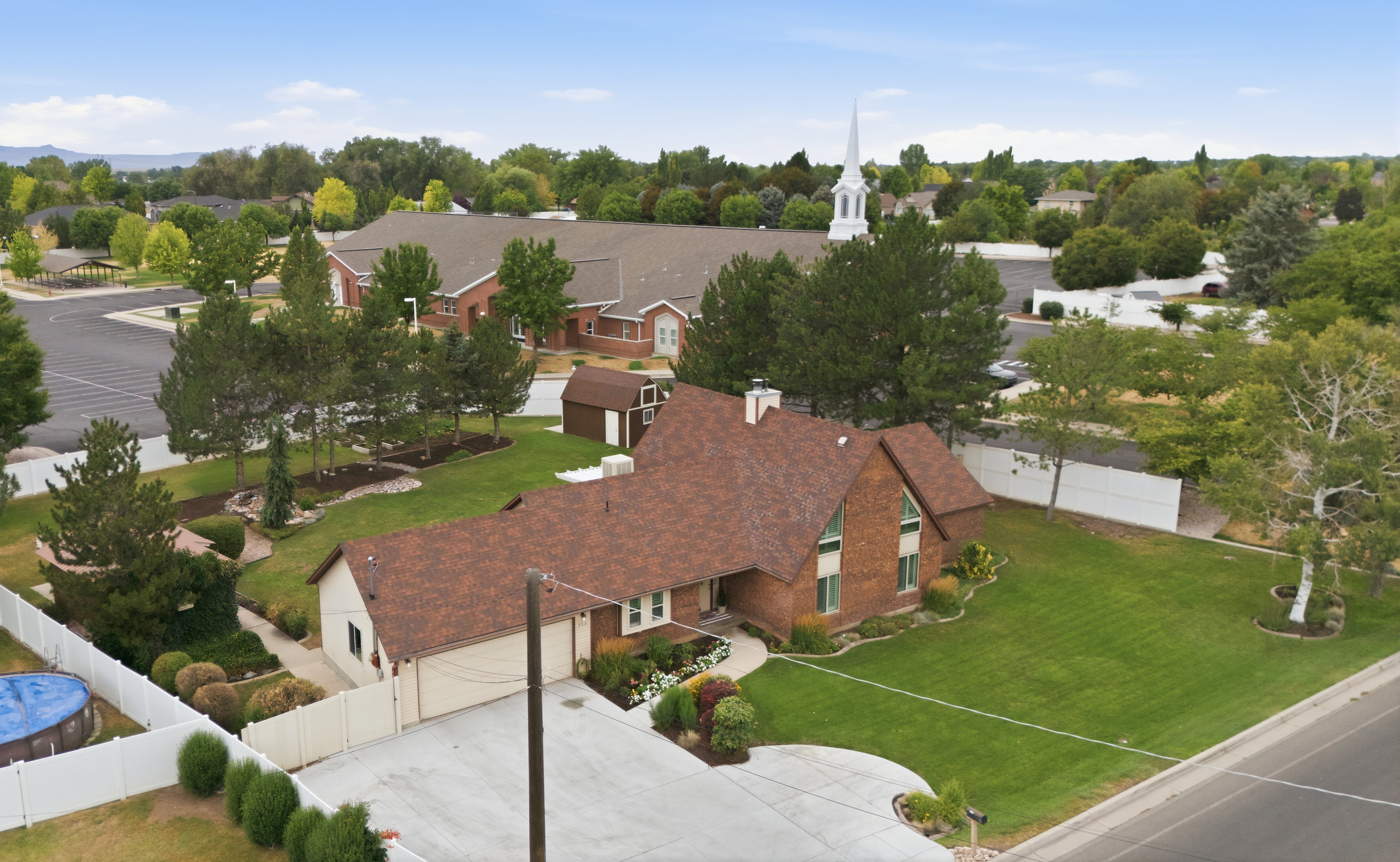 Expansive property featuring a red brick exterior, a large asphalt shingle roof, established landscaping, and a manicured lawn