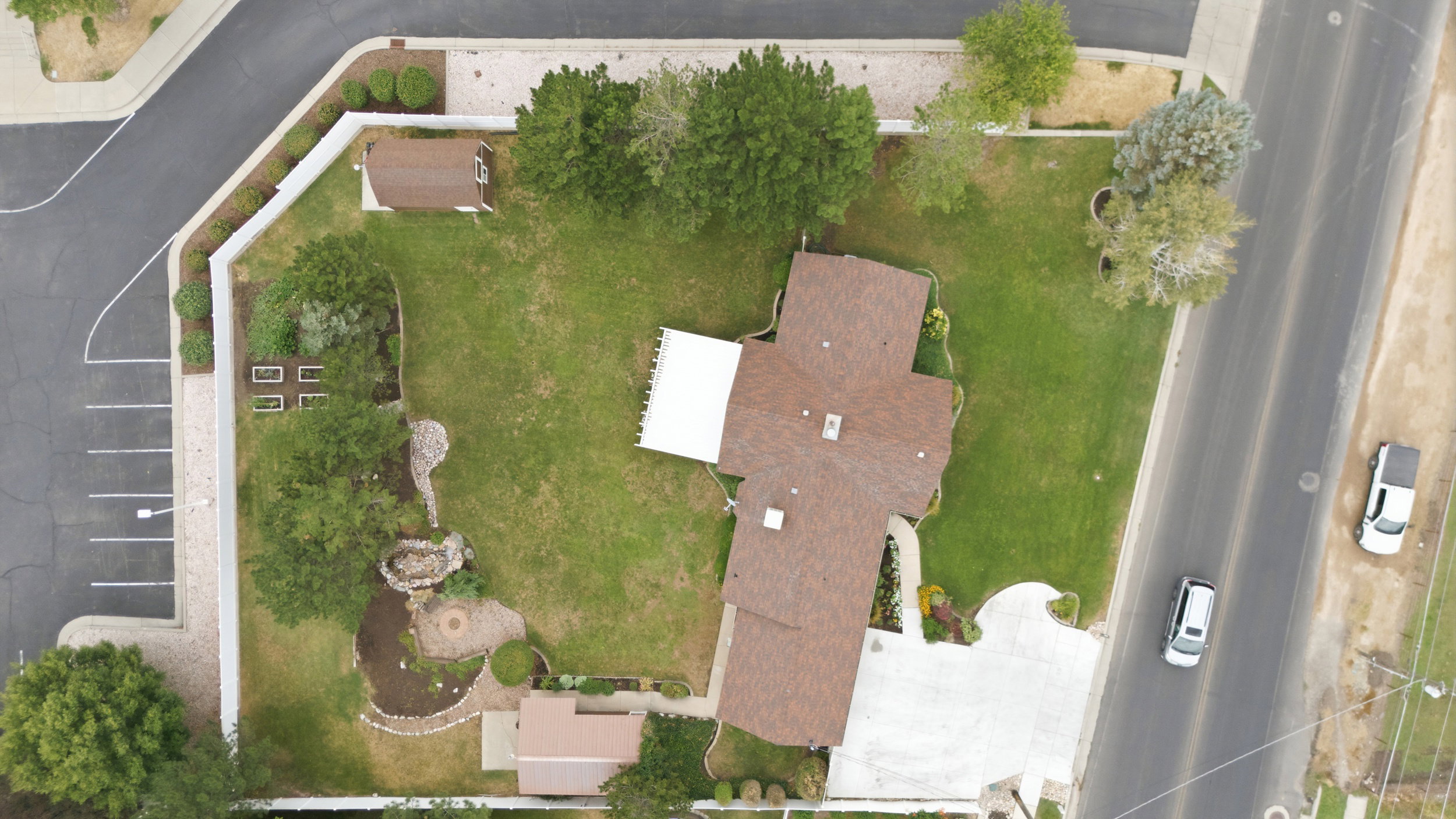 Expansive property featuring a brown shingle roofline, concrete driveway, and a spacious green lawn