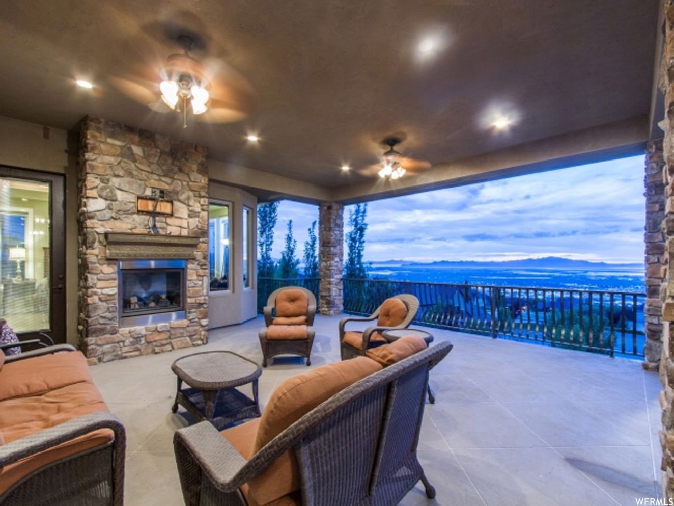 Expansive covered patio featuring a stone-clad fireplace, recessed lighting, and ceiling fans