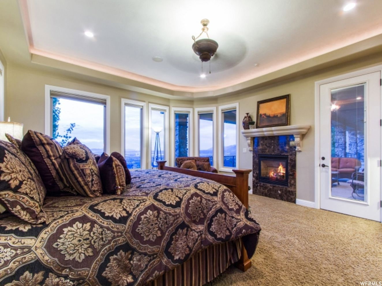 Room featuring a bay window wall, tray ceiling with recessed lighting, and a dark stone fireplace with a light-colored mantel