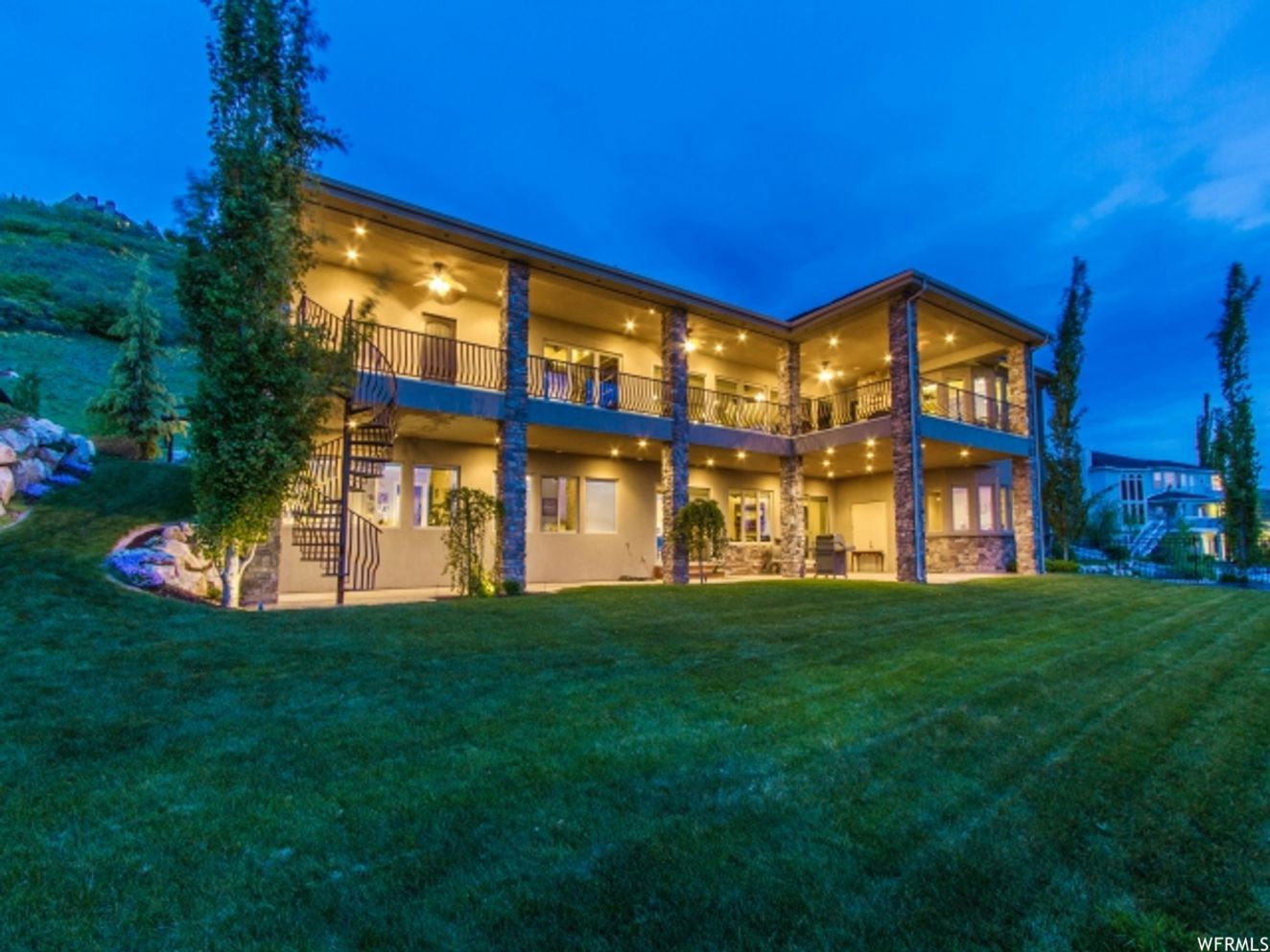 Two-story exterior featuring stone columns, covered patios on both levels, and a spiral staircase