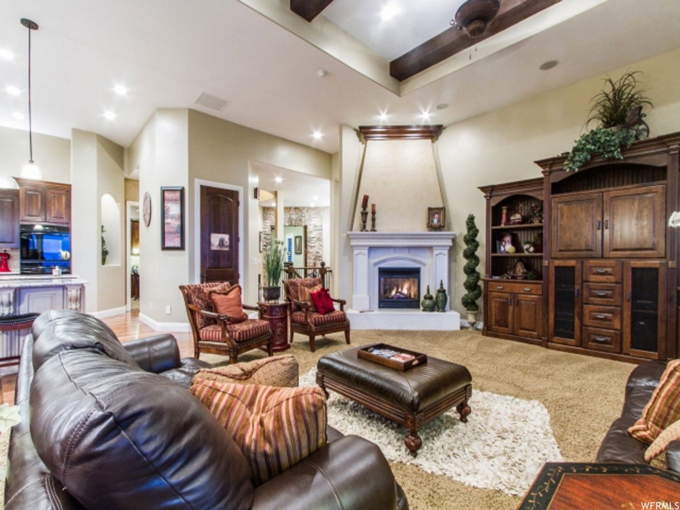 Living area featuring a gas fireplace with a decorative mantelpiece, recessed lighting, a ceiling fan, exposed wood beams, and carpeted flooring