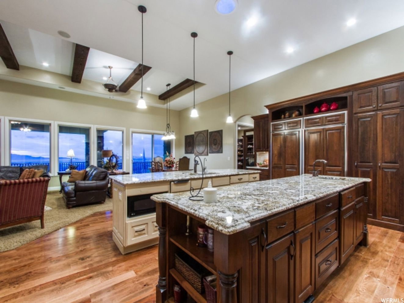 Open-concept kitchen and living area featuring dual islands with granite countertops, rich wood-finish flooring, and exposed ceiling beams
