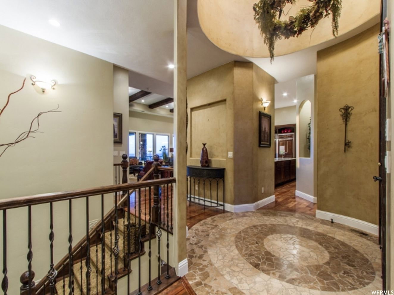 Foyer featuring a mosaic tile floor with a circular pattern, arched doorways, a wrought iron staircase with wood handrails, recessed lighting, and sconce lighting