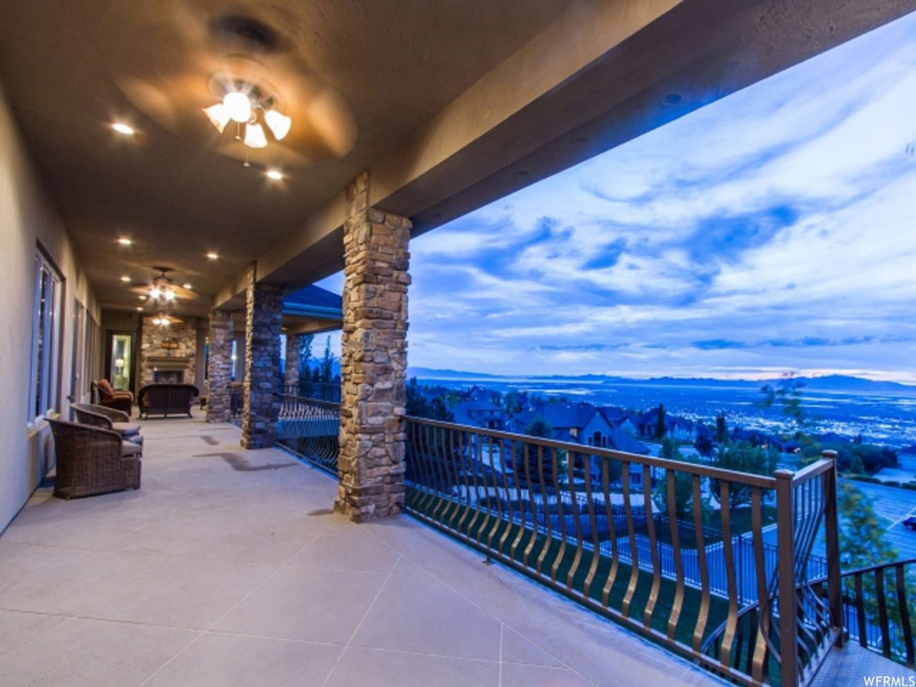 Expansive covered patio featuring stone-clad columns, recessed lighting, and ceiling fans