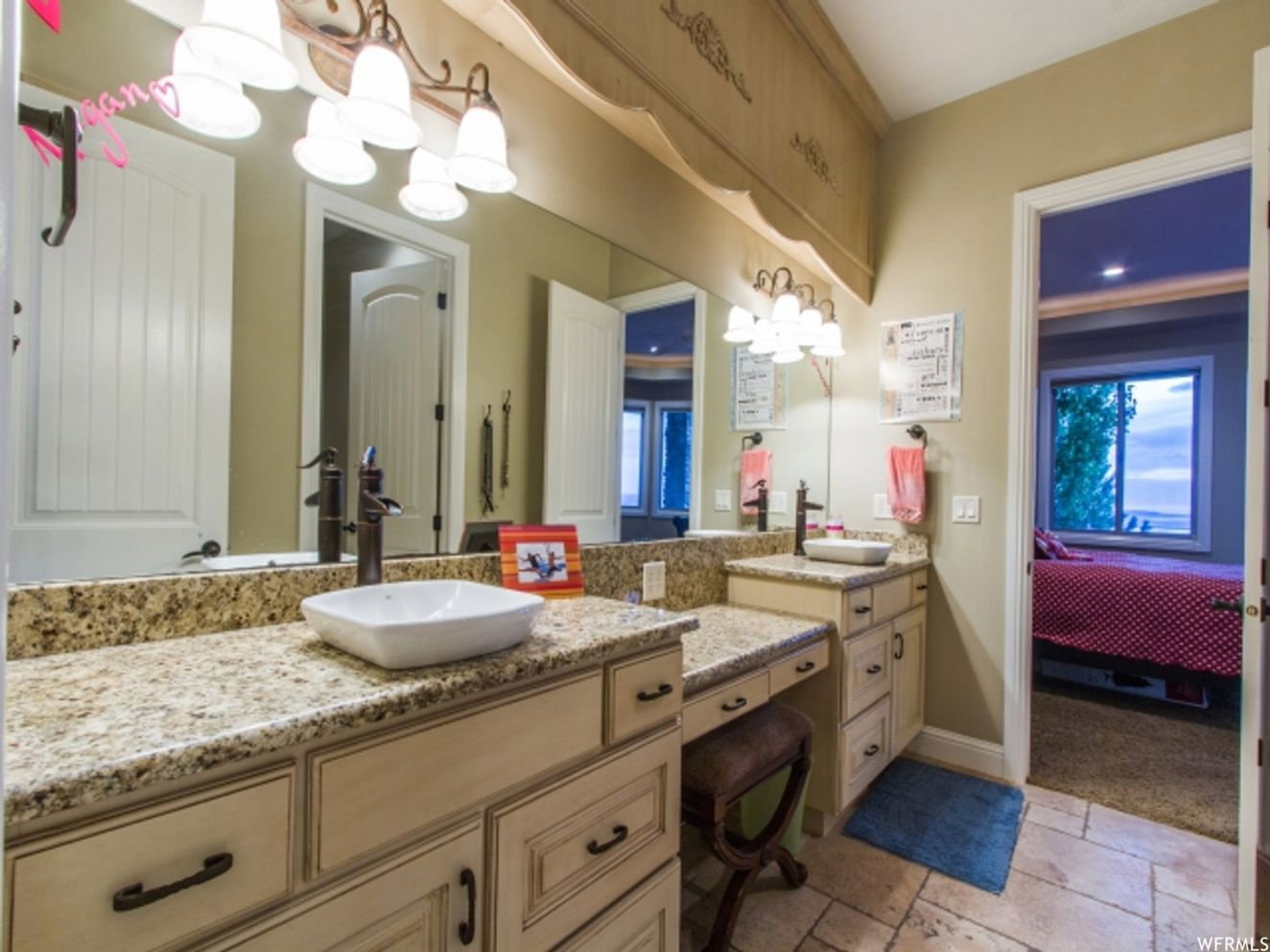 Bathroom vanity featuring dual vessel sinks, stone countertops, and cream-toned cabinetry with dark hardware