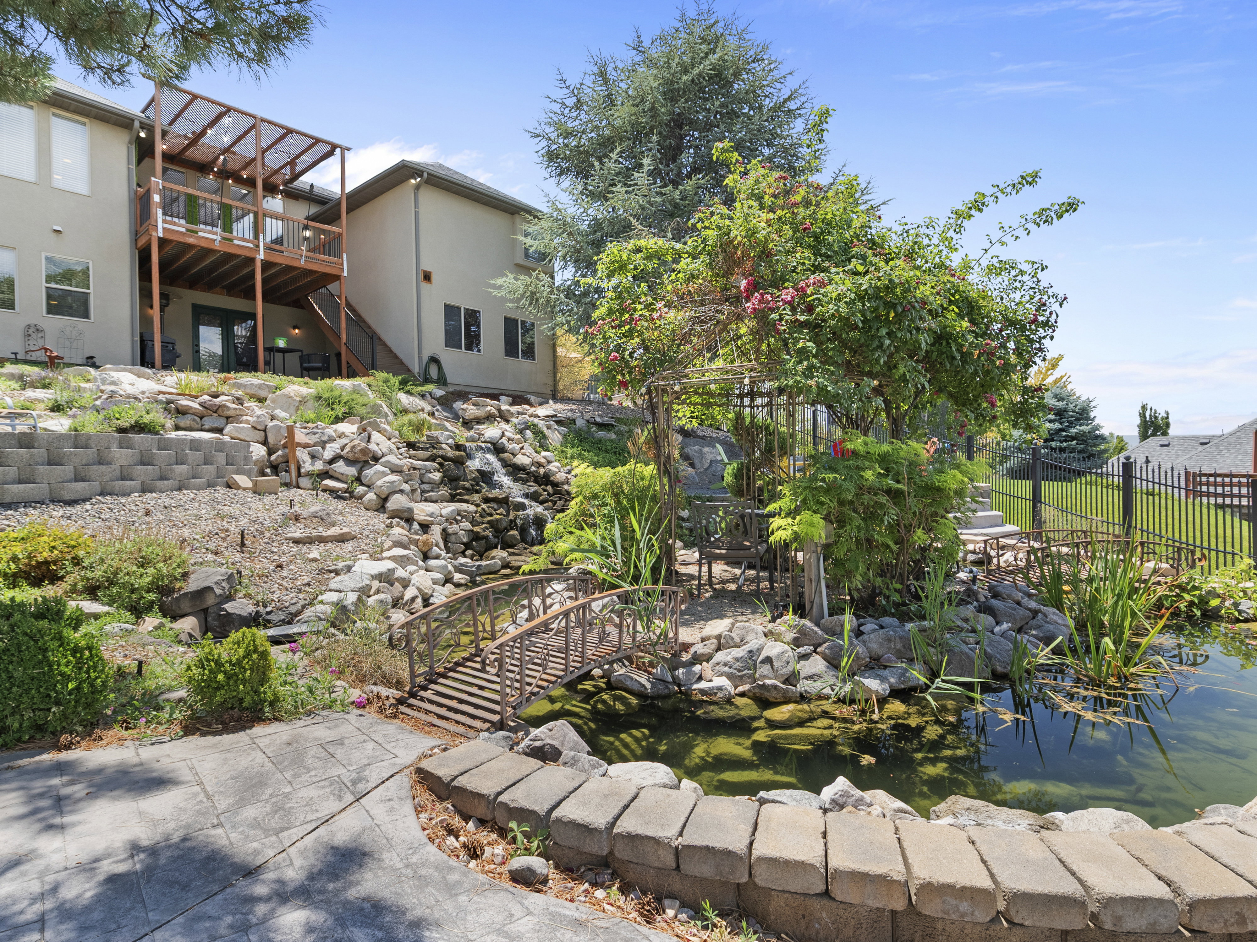 Terraced backyard featuring a multi-level deck with a pergola, a stone waterfall, a pond with a decorative bridge, and a stamped concrete patio