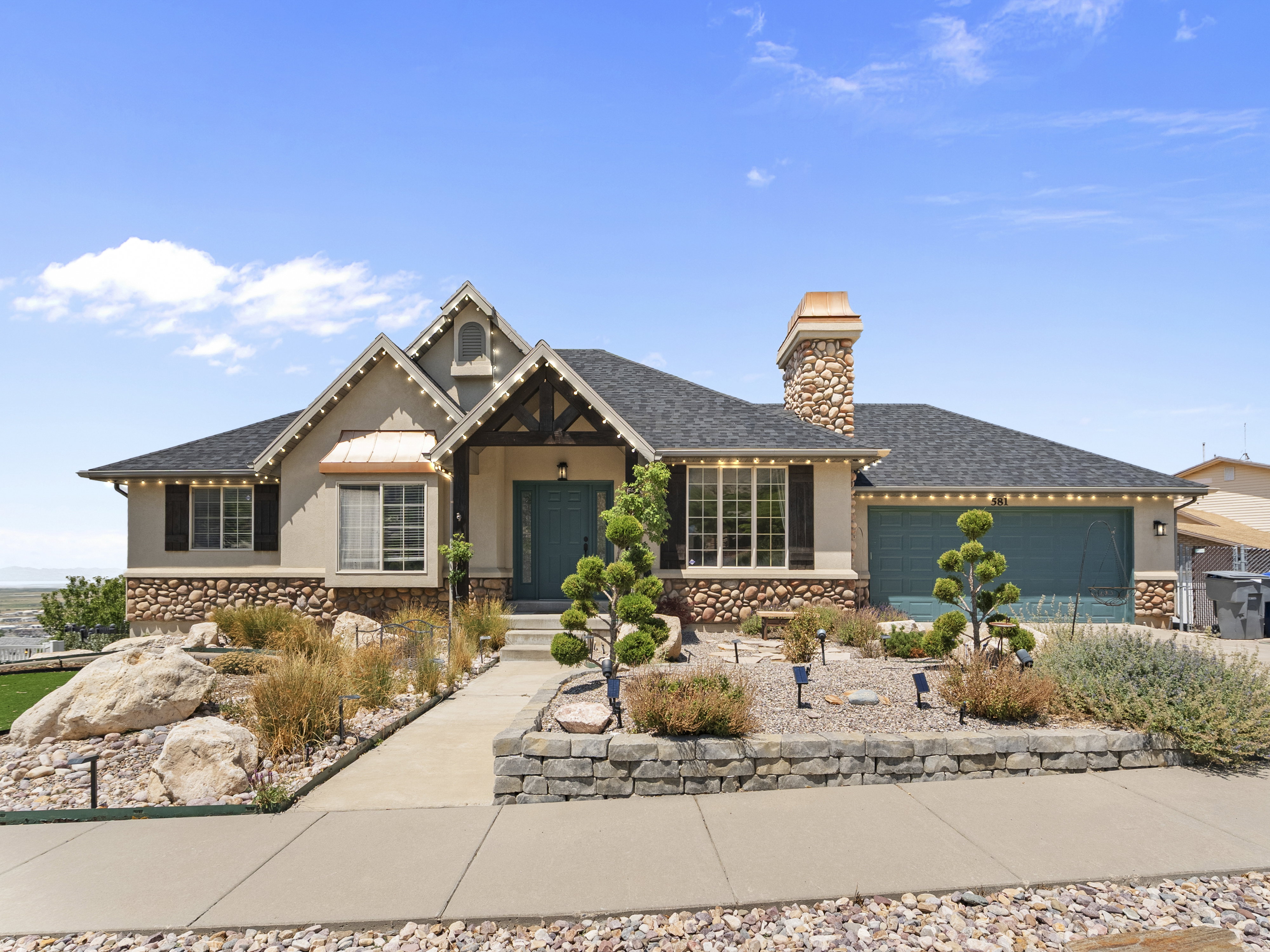 Craftsman-style exterior featuring a turquoise front door, stone chimney, copper window awning, and a two-car garage
