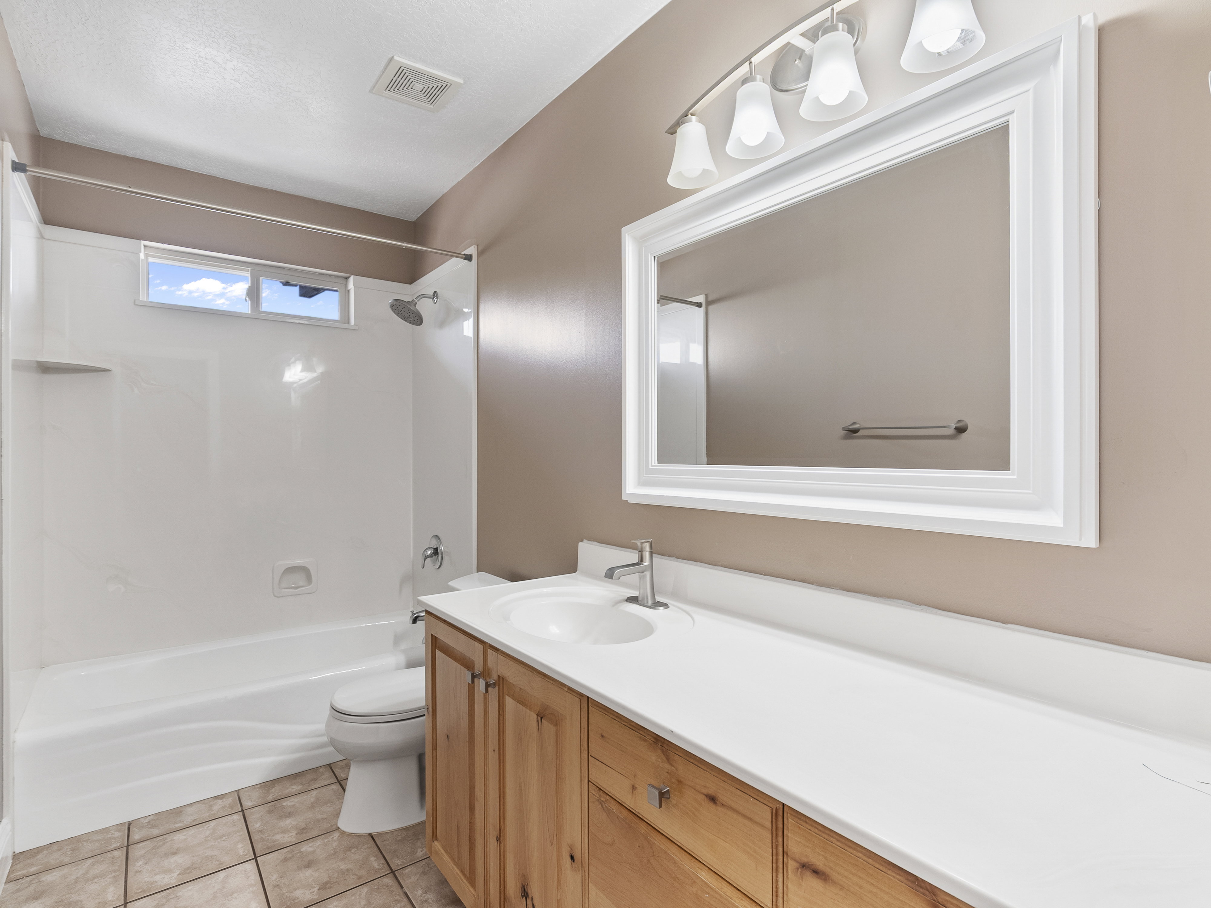 Bathroom featuring a white vanity top, wood-finish cabinetry, and a framed mirror with overhead lighting