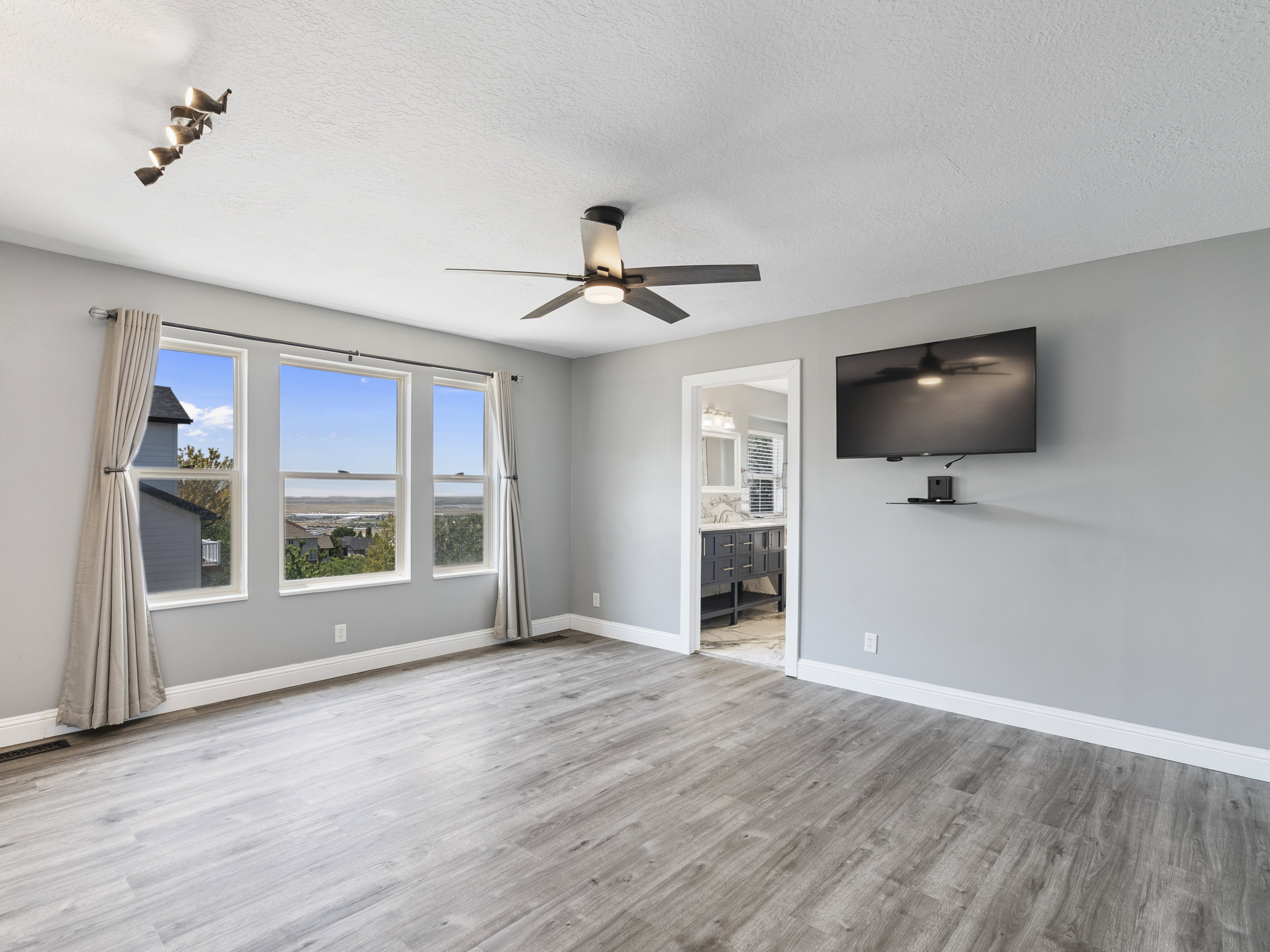 Spacious interior room featuring wood-finish flooring, a contemporary ceiling fan, and multiple windows