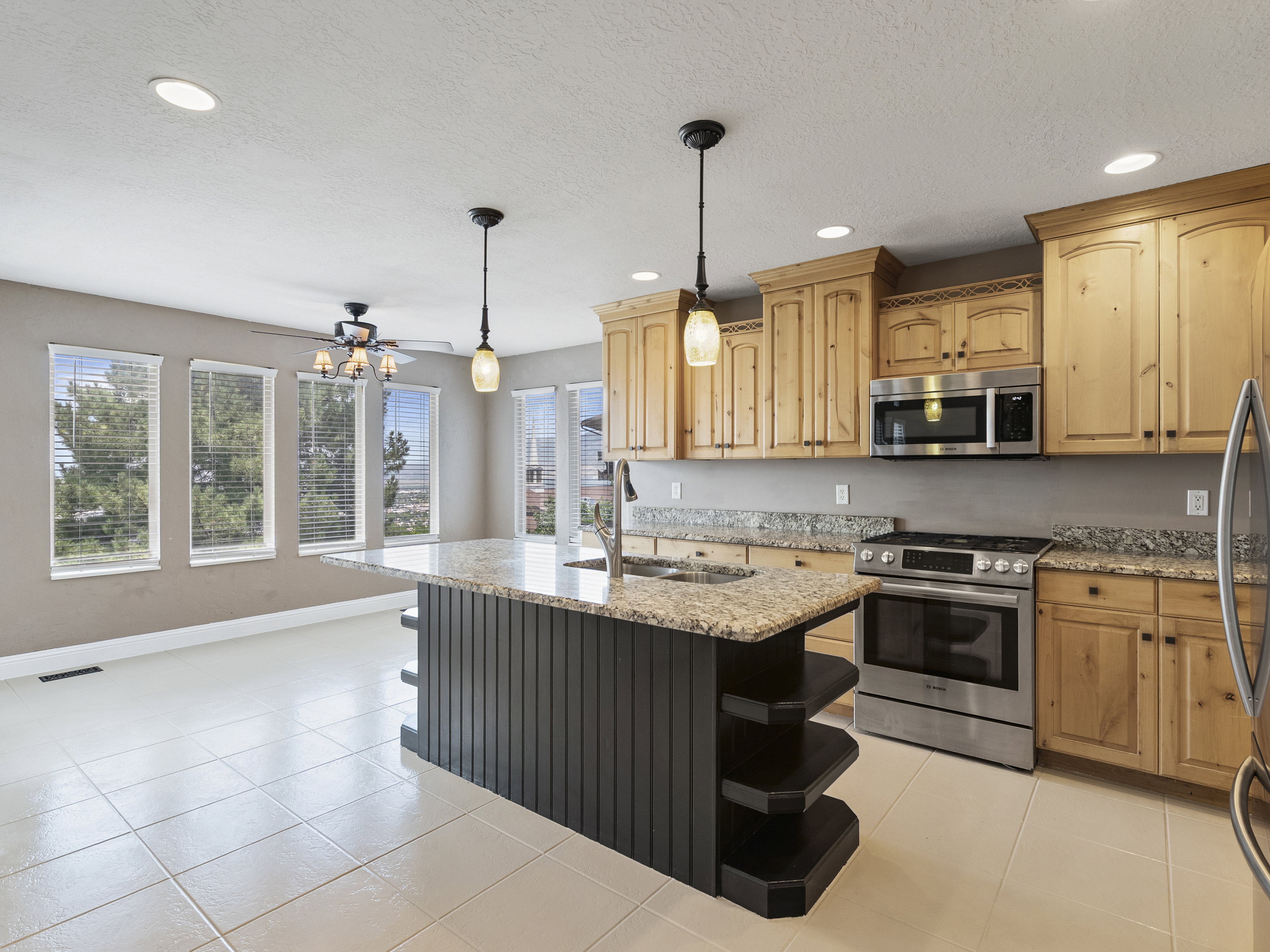 Spacious kitchen featuring an island with a sink, light wood cabinetry, stainless steel appliances, and ample natural light from multiple windows
