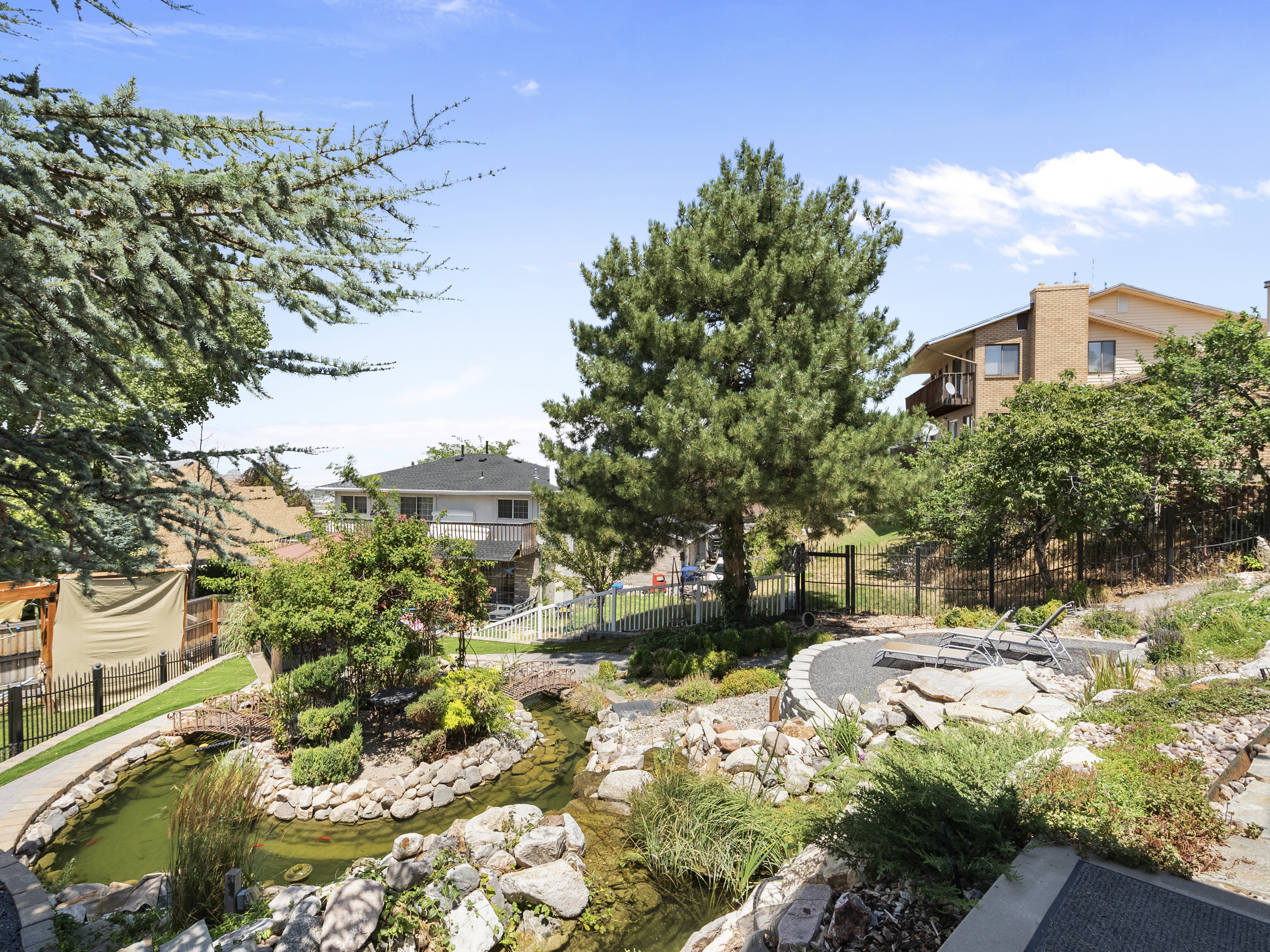 Tiered landscaping featuring a serene pond with two footbridges, surrounded by mature trees and natural rock formations