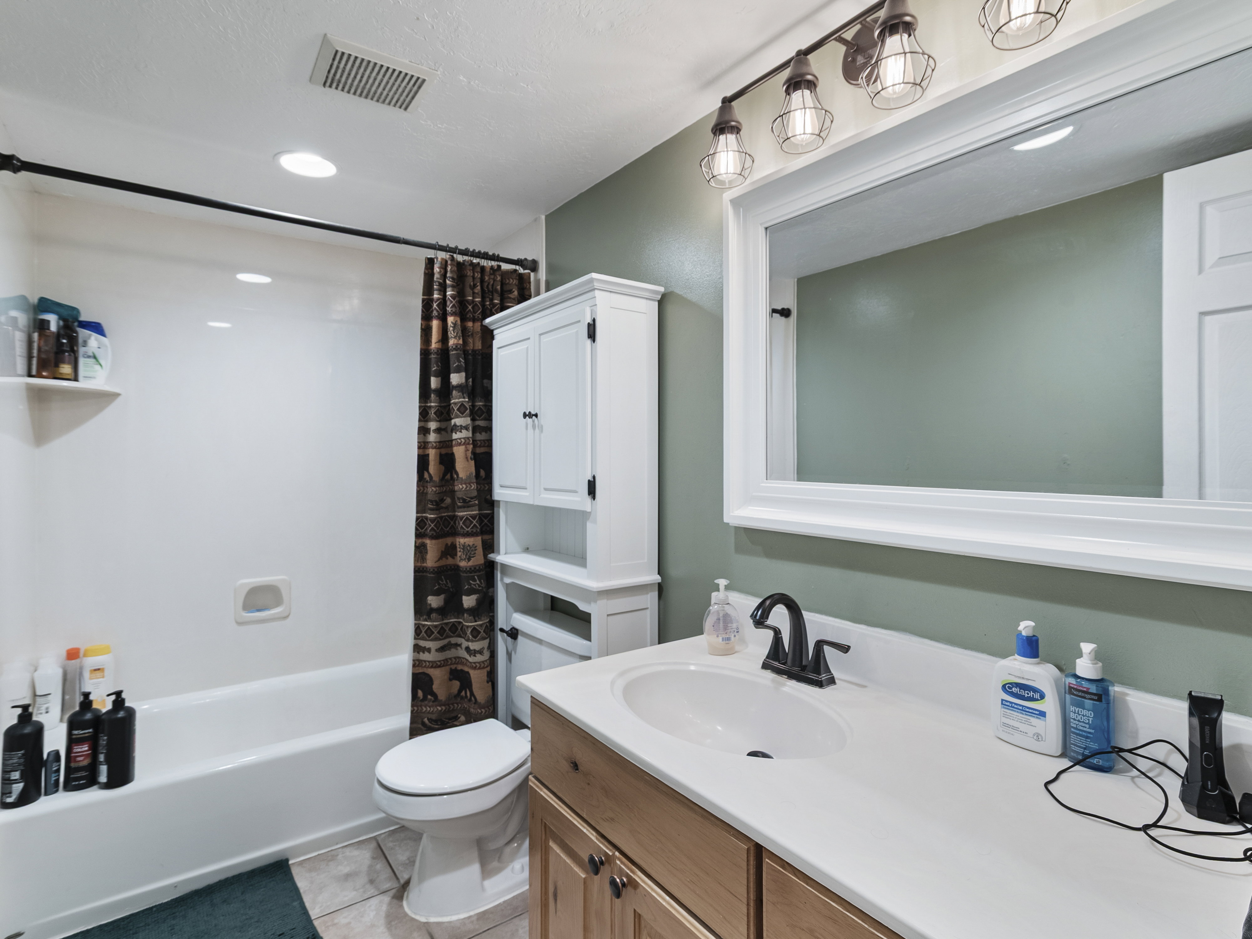Bathroom featuring a white bathtub with a shower, a wood-finish vanity with a white countertop and integrated sink, a large framed mirror, and track lighting with wire cage fixtures