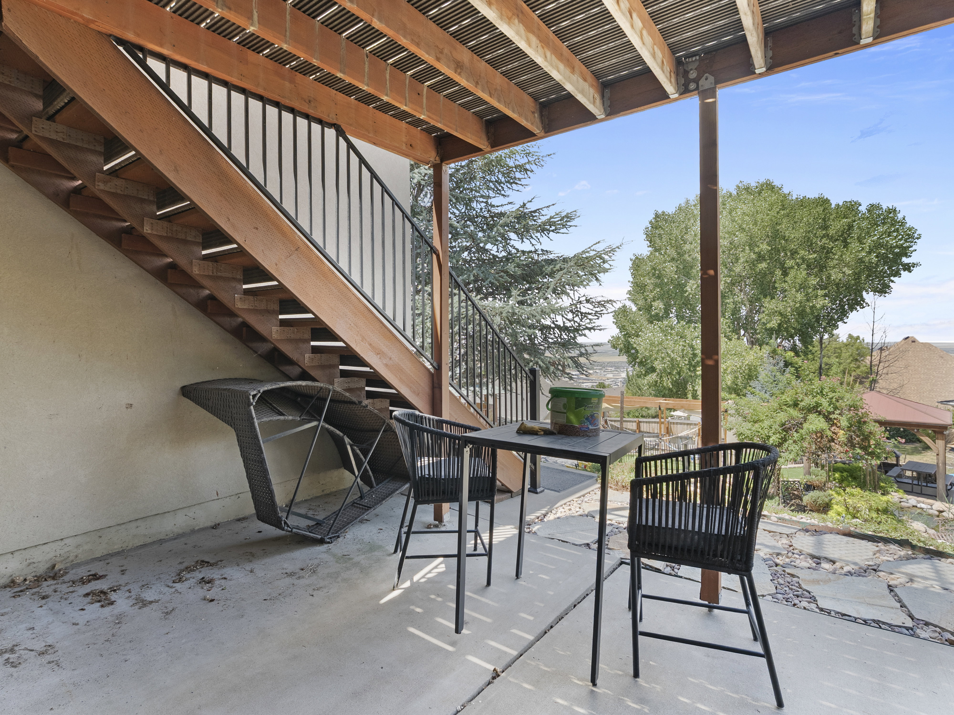Concrete patio area featuring a wooden deck structure overhead and a staircase with black metal railings
