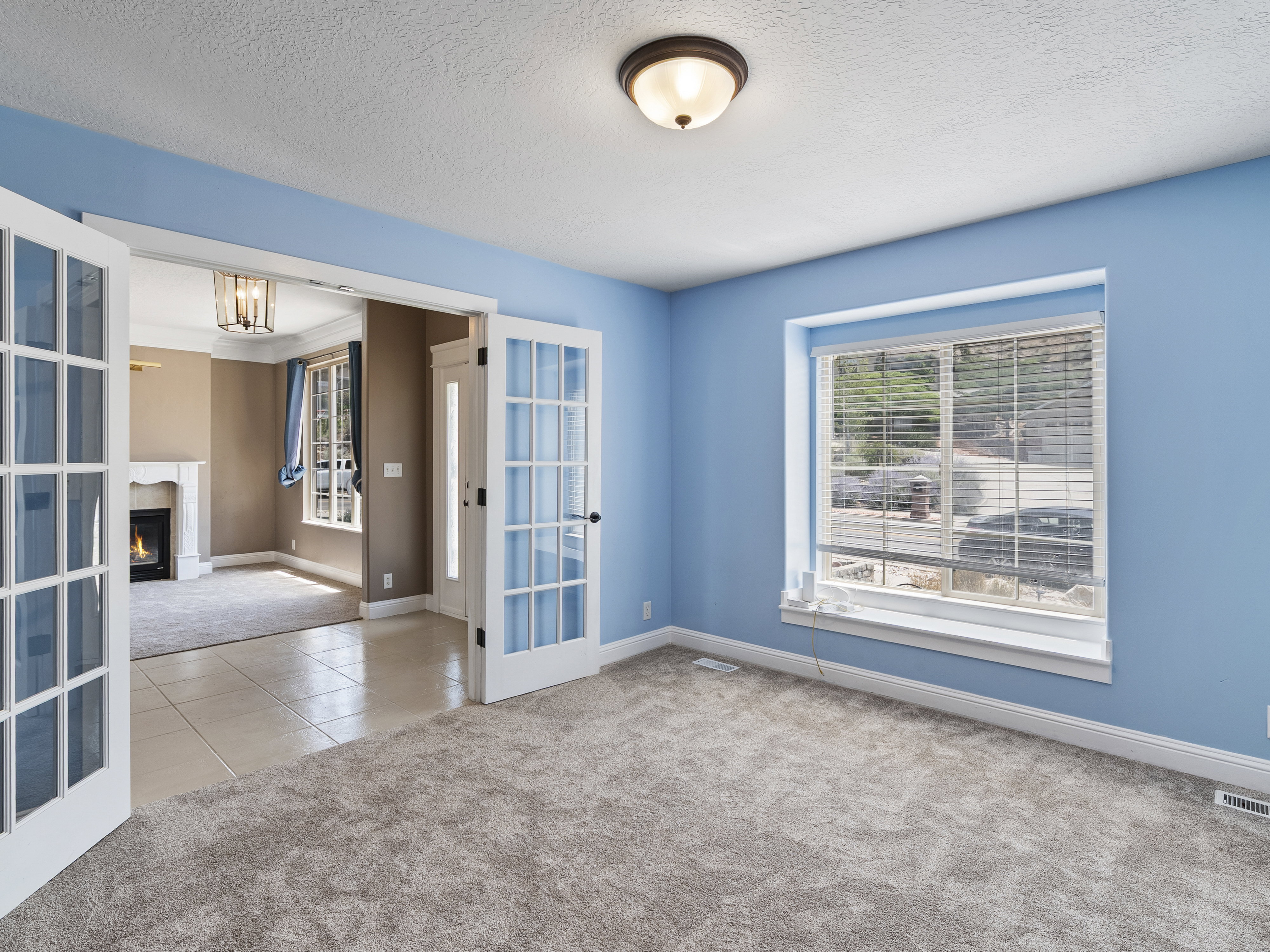 Carpeted room featuring a large window with blinds, French doors, and ceiling-mounted lighting