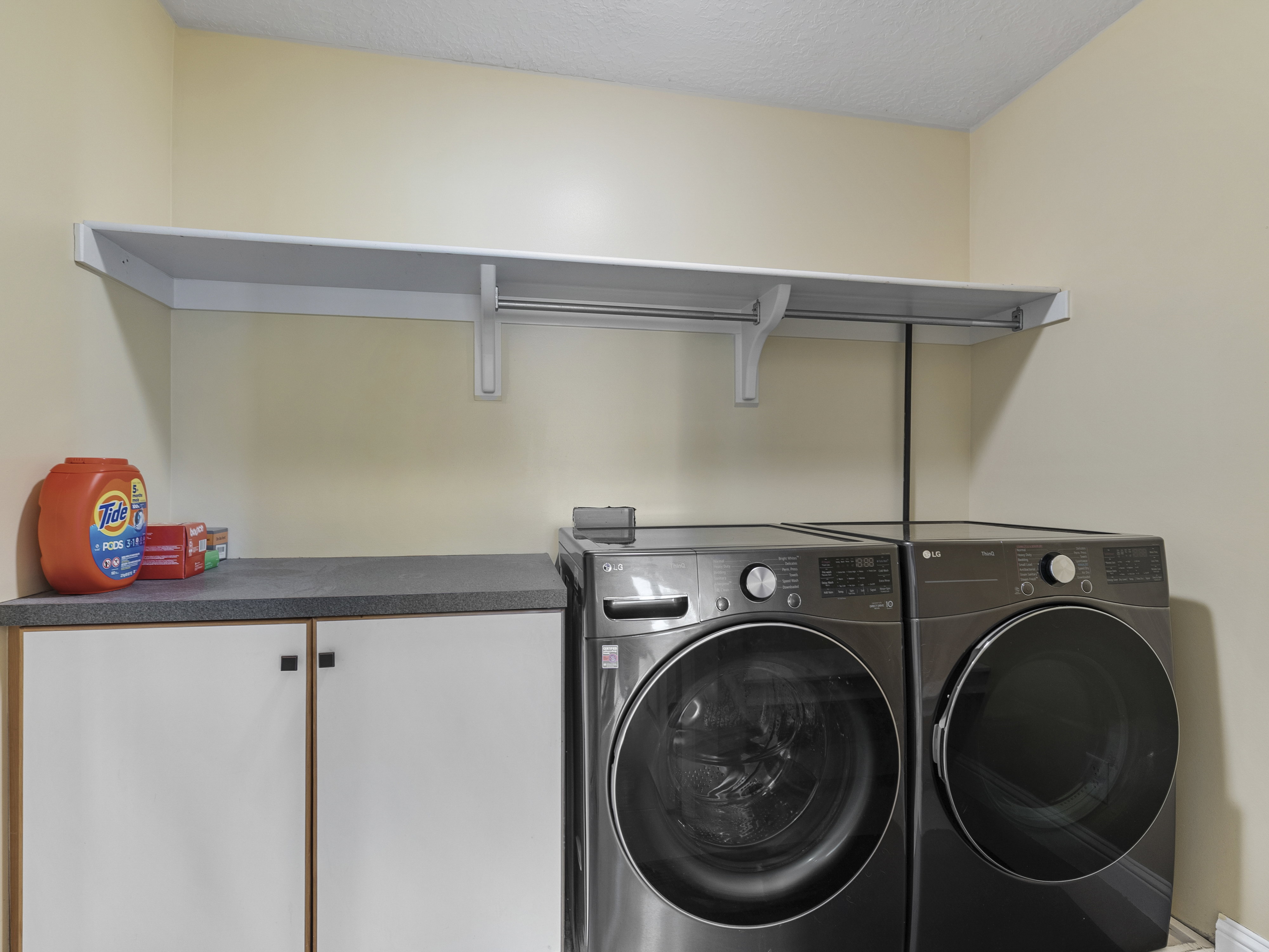 Dedicated laundry area featuring a built-in white shelf with a hanging rod, a dark countertop, and white cabinetry with dark hardware