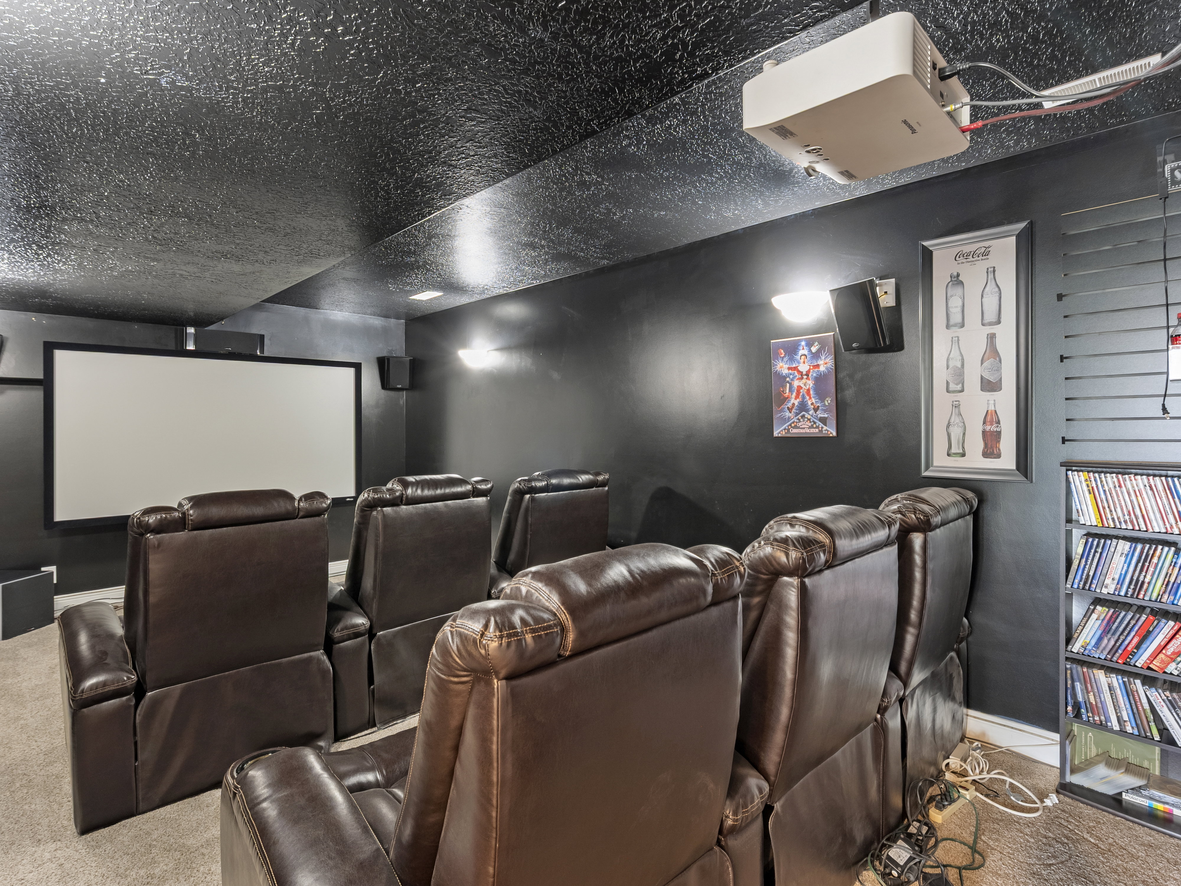 Dedicated media room featuring a large projection screen, wall-mounted speakers, and recessed lighting