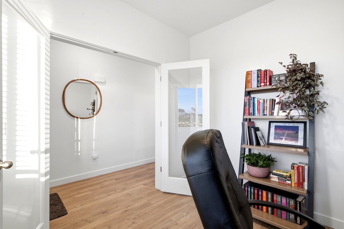 Bright interior space featuring wood-finish flooring, white walls, and a white interior door with louvered blinds