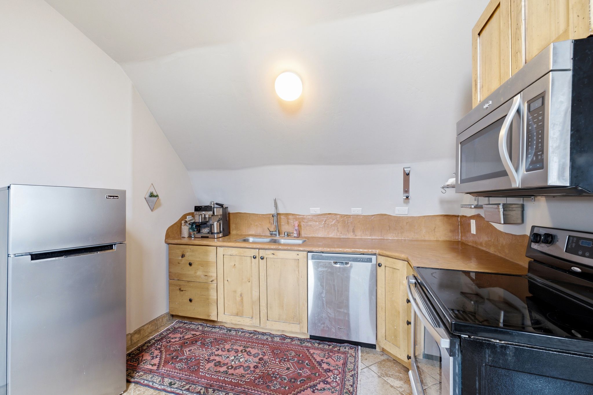 Compact kitchen featuring stainless steel appliances including a refrigerator, microwave, and dishwasher