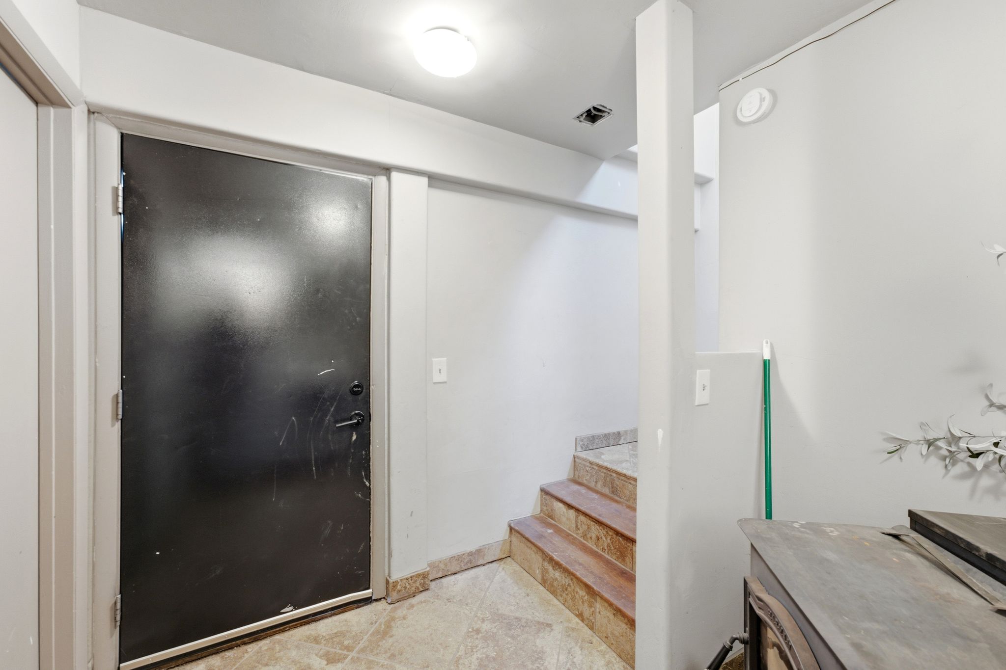 Entry area featuring a dark-paneled door, recessed lighting, and a partial view of interior stairs with stone-finish treads