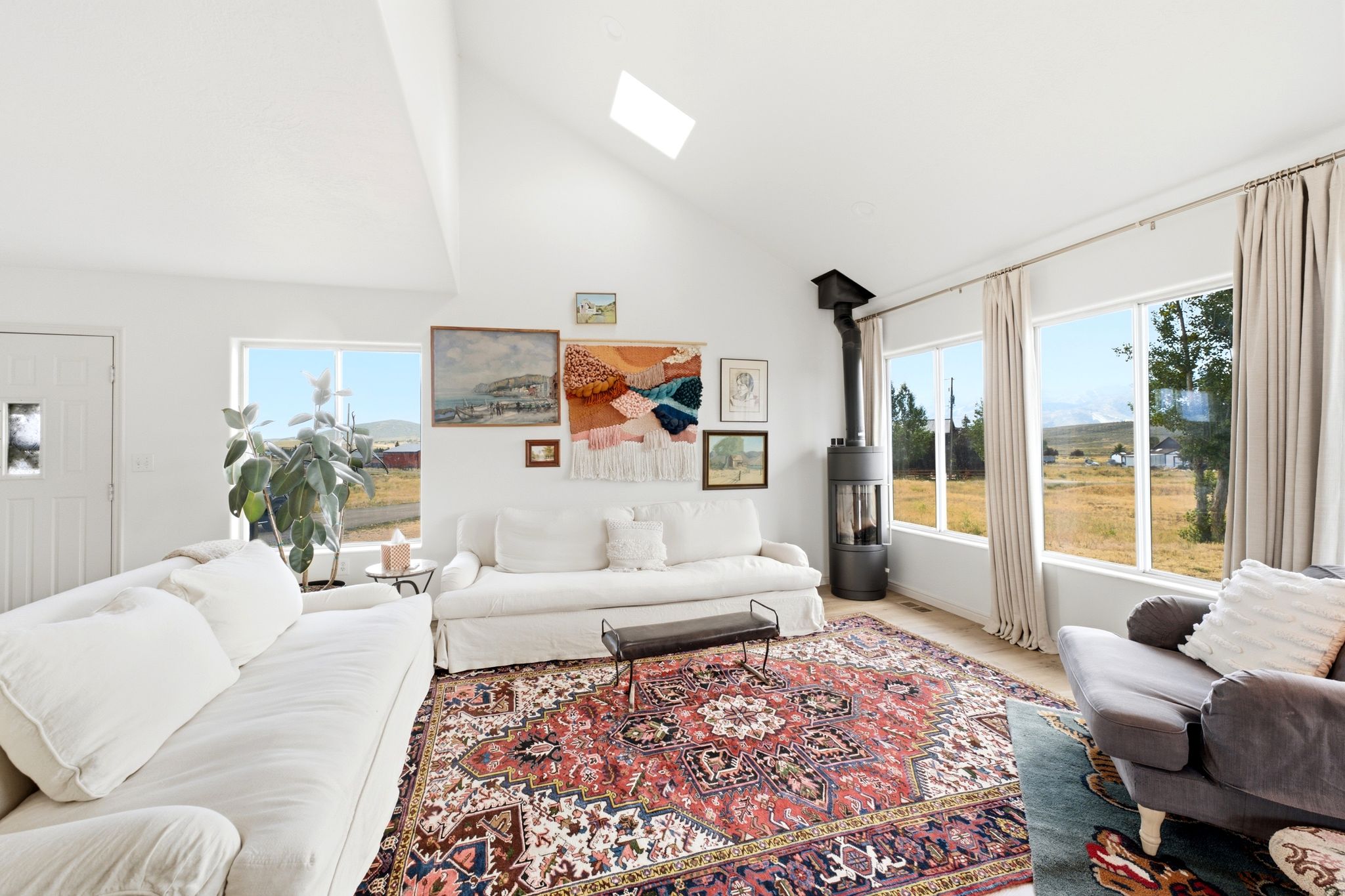 Spacious living area featuring a vaulted ceiling with skylight, extensive window line, wood-finish flooring, and a freestanding wood-burning stove