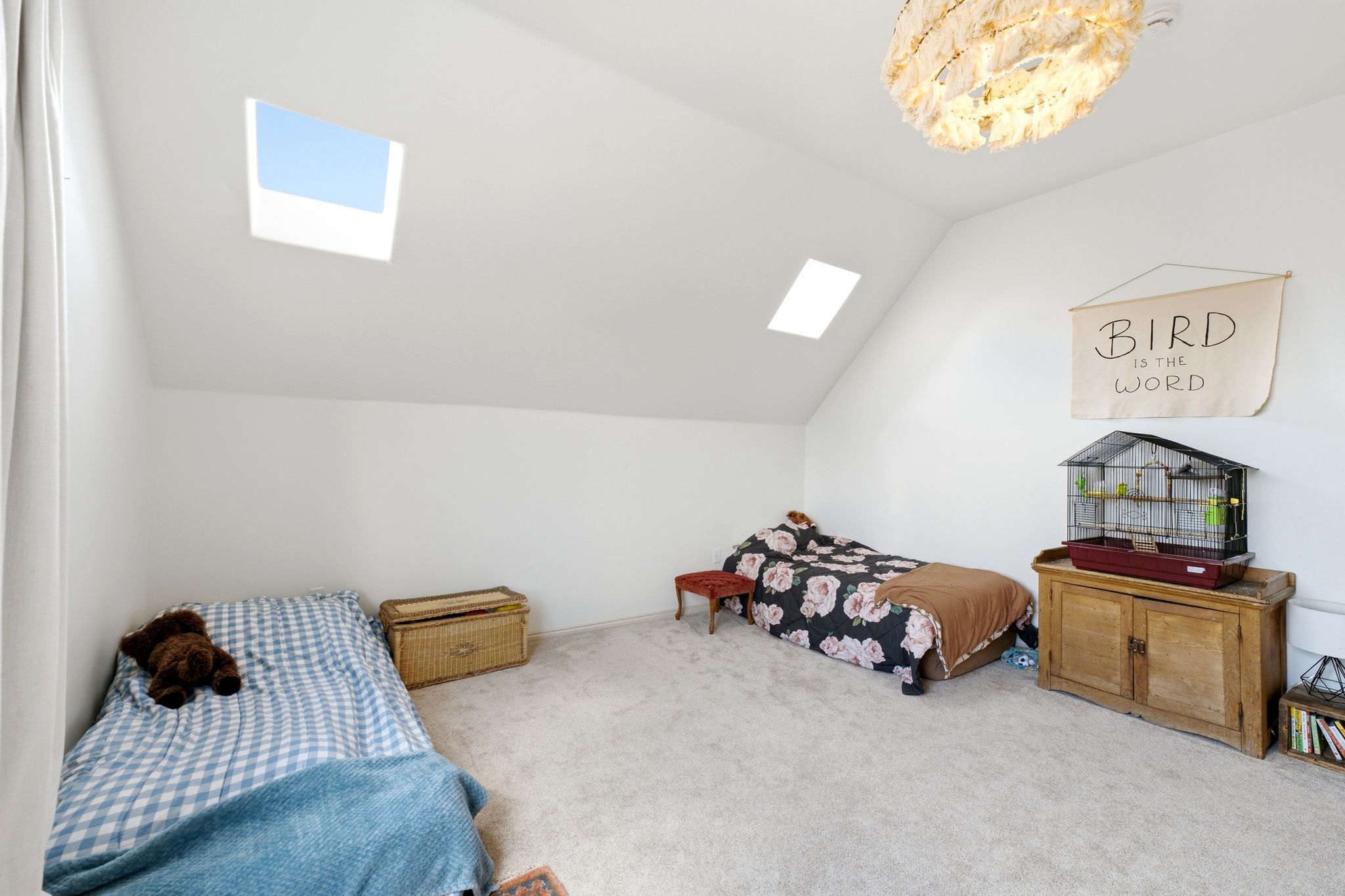 Light-filled room featuring sloped ceilings, two skylights, and neutral carpet flooring
