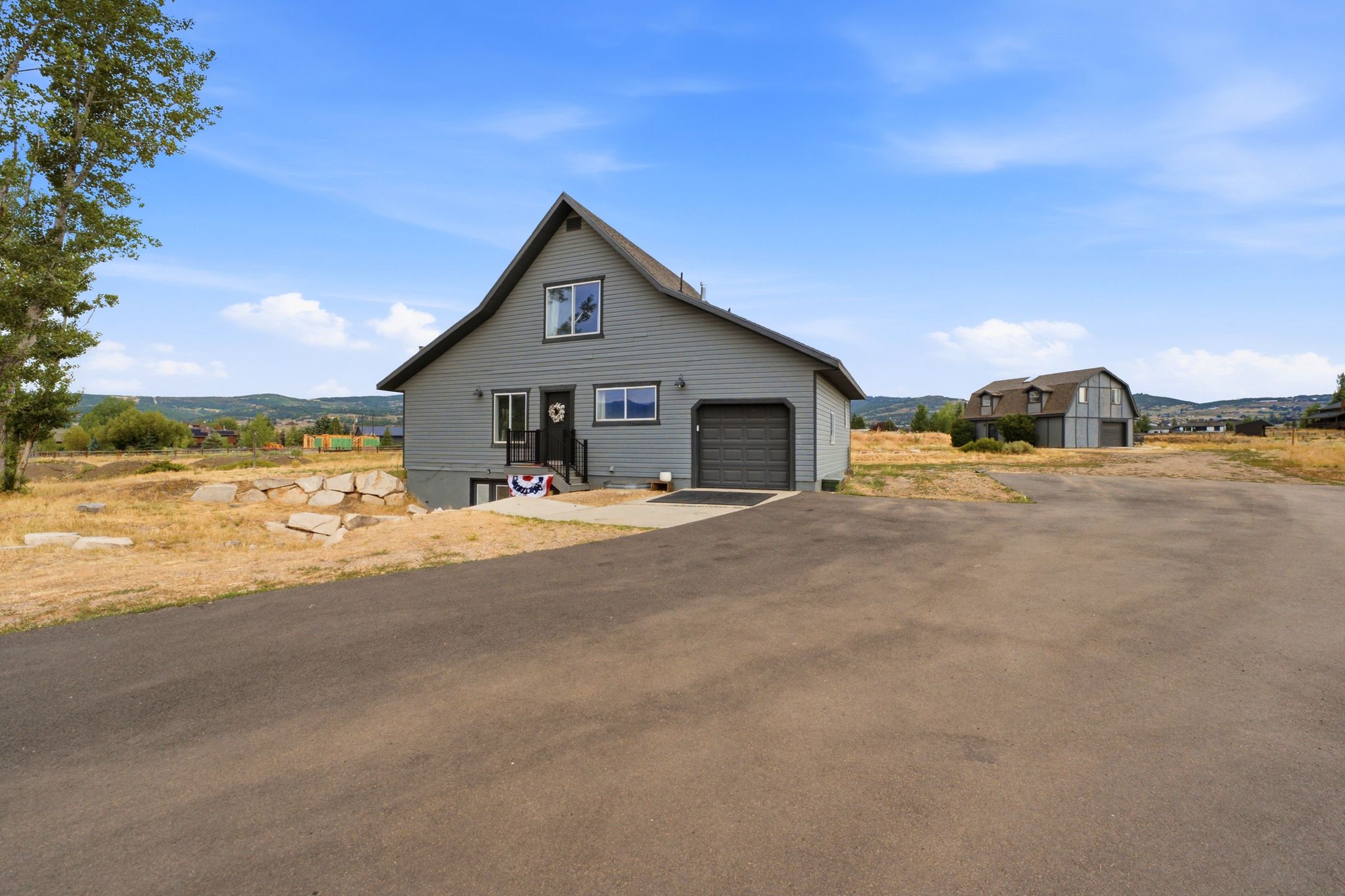 Gray siding exterior featuring a single-car garage with an asphalt driveway and a stone retaining wall