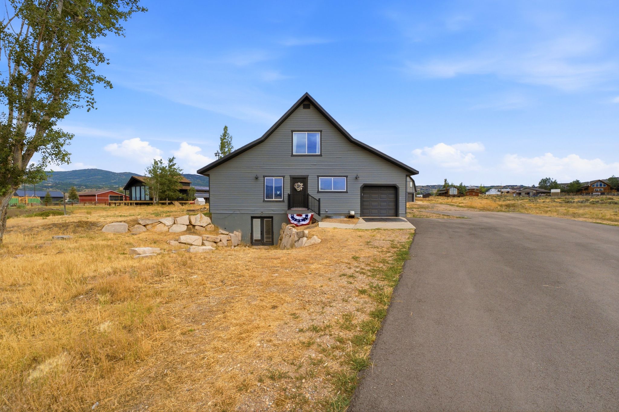 Barn-style exterior featuring gray siding, a black shingled roof, and a single-car garage with a paneled door