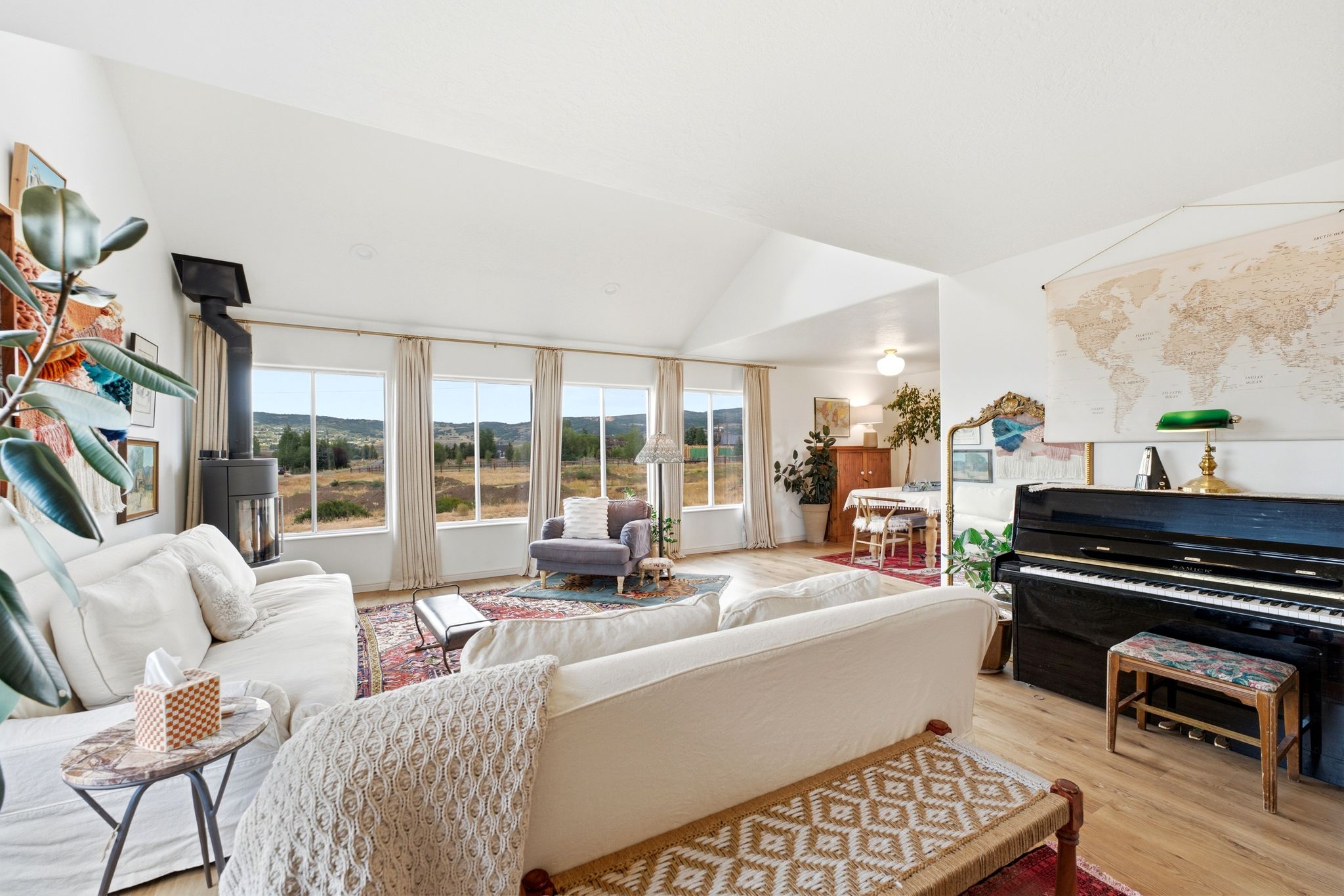 Vaulted ceilings crowning a spacious living area featuring wood-finish flooring, a contemporary black wood-burning stove, and multiple large windows showcasing distant landscapes