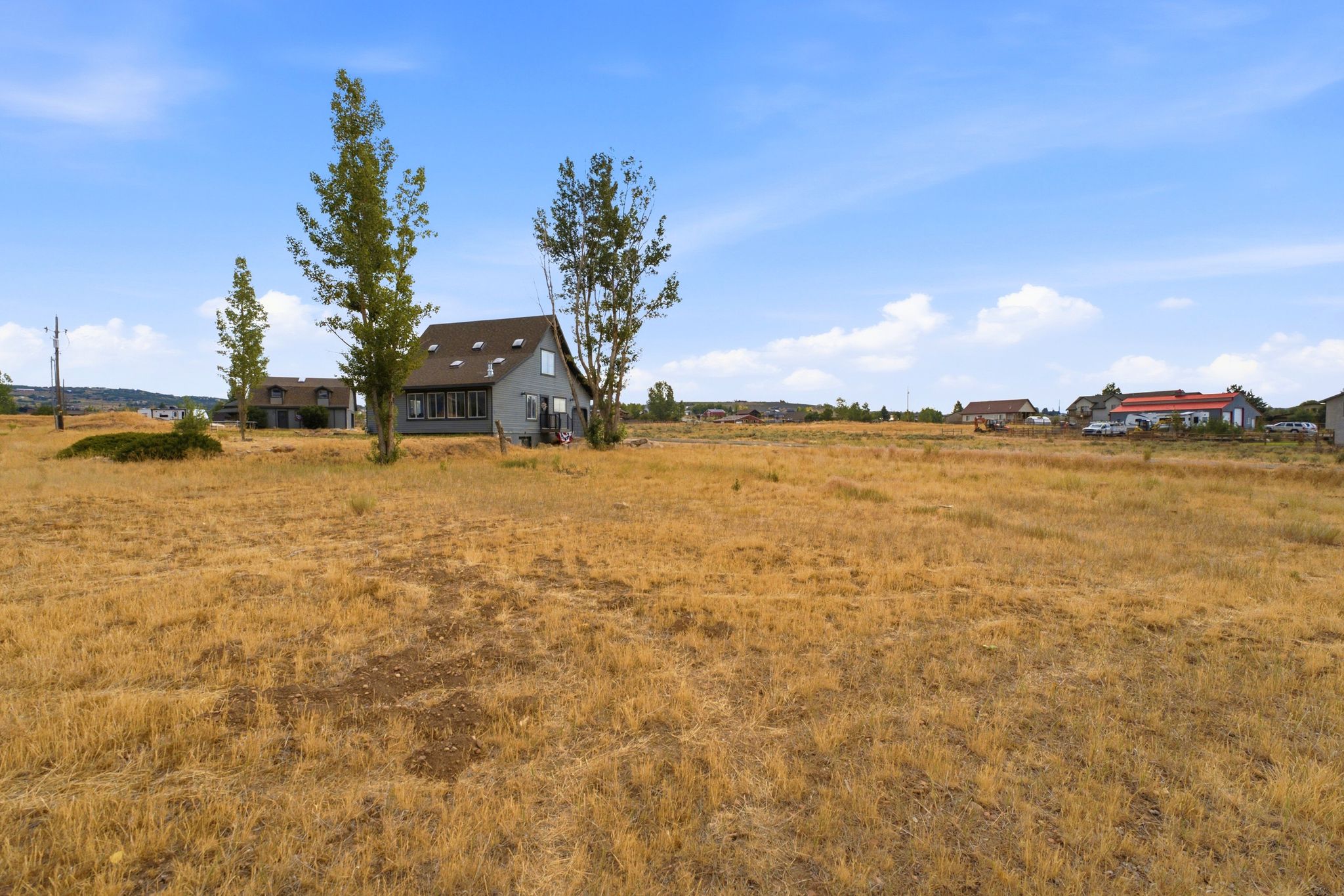 Expansive open land featuring a detached residential structure with a gray facade, multiple windows, and a dark shingle roof with skylights