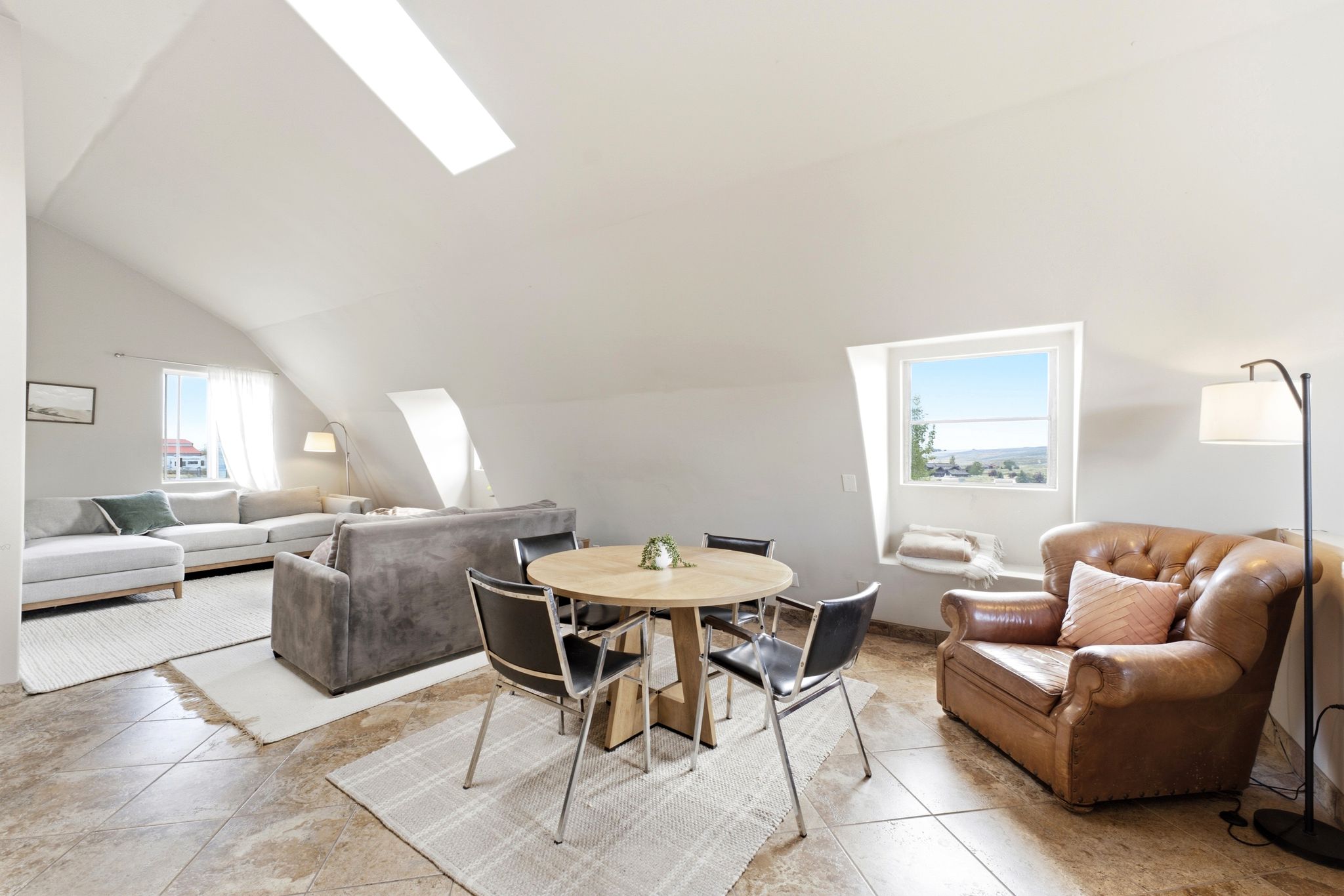 Spacious vaulted ceiling room featuring a skylight, tile flooring, and multiple windows