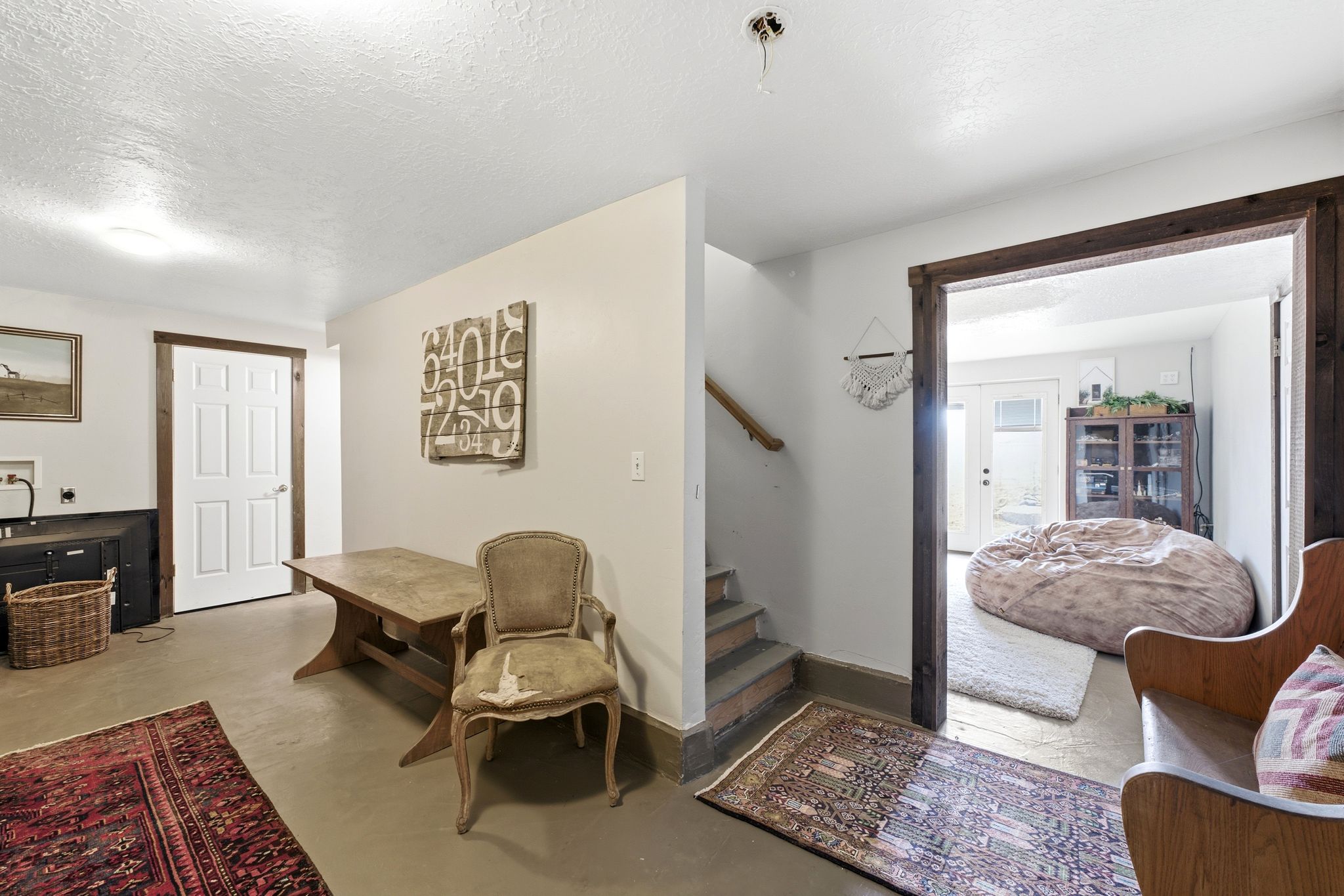 Finished lower level space featuring a white paneled door, wood trim accents, and a staircase with a wood handrail