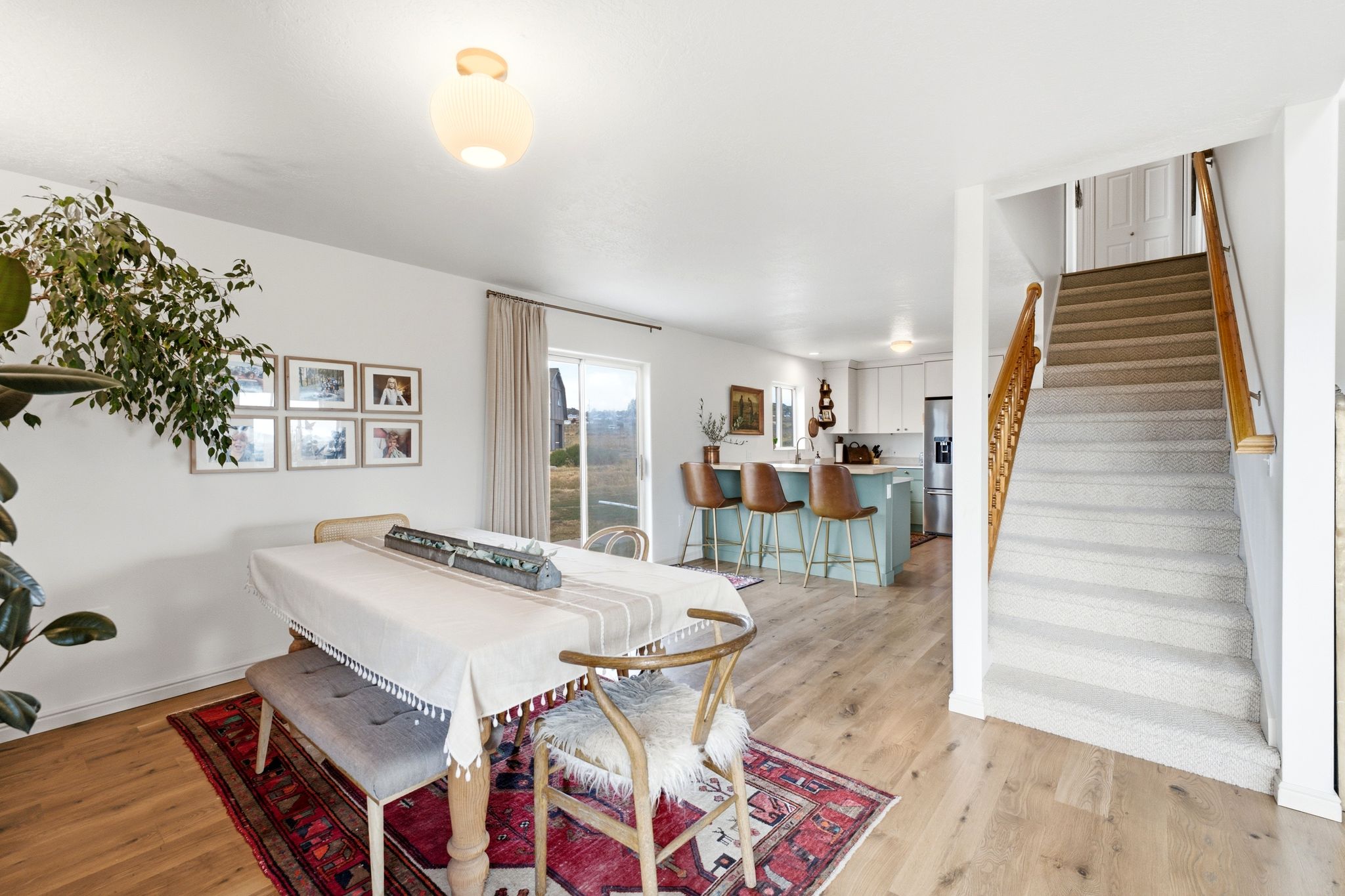Open-concept living area featuring wood-finish flooring, a contemporary kitchen island with seating, white cabinetry, stainless steel appliances, and a carpeted staircase with wood railings