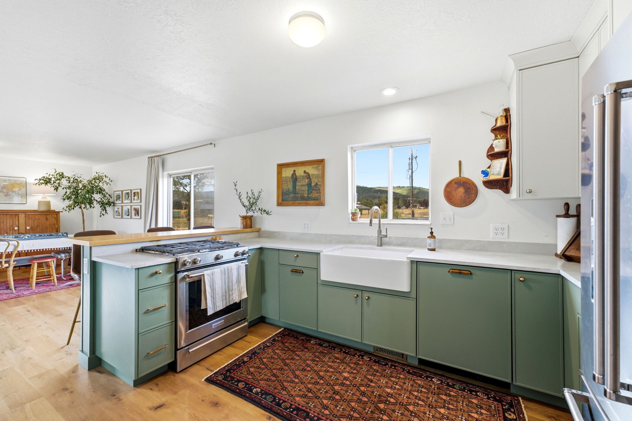 Kitchen featuring sage green lower cabinetry, wood-finish flooring, a farmhouse sink, stainless steel appliances, and light-toned countertops