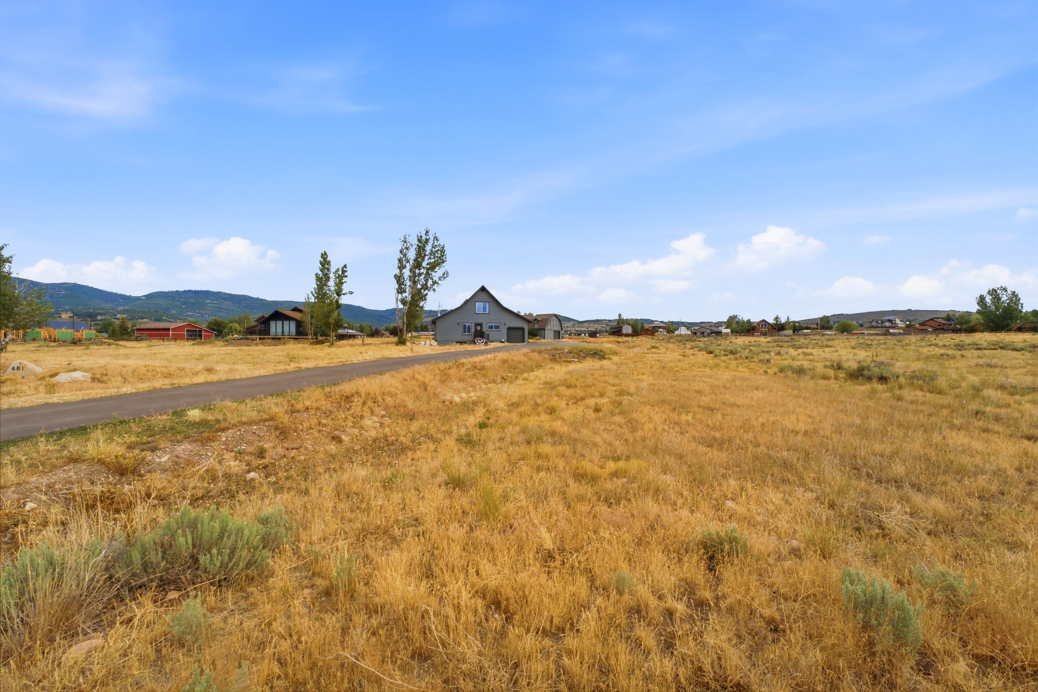 Contemporary gray exterior with a pitched roof, featuring a paved driveway, and surrounded by open, undeveloped land
